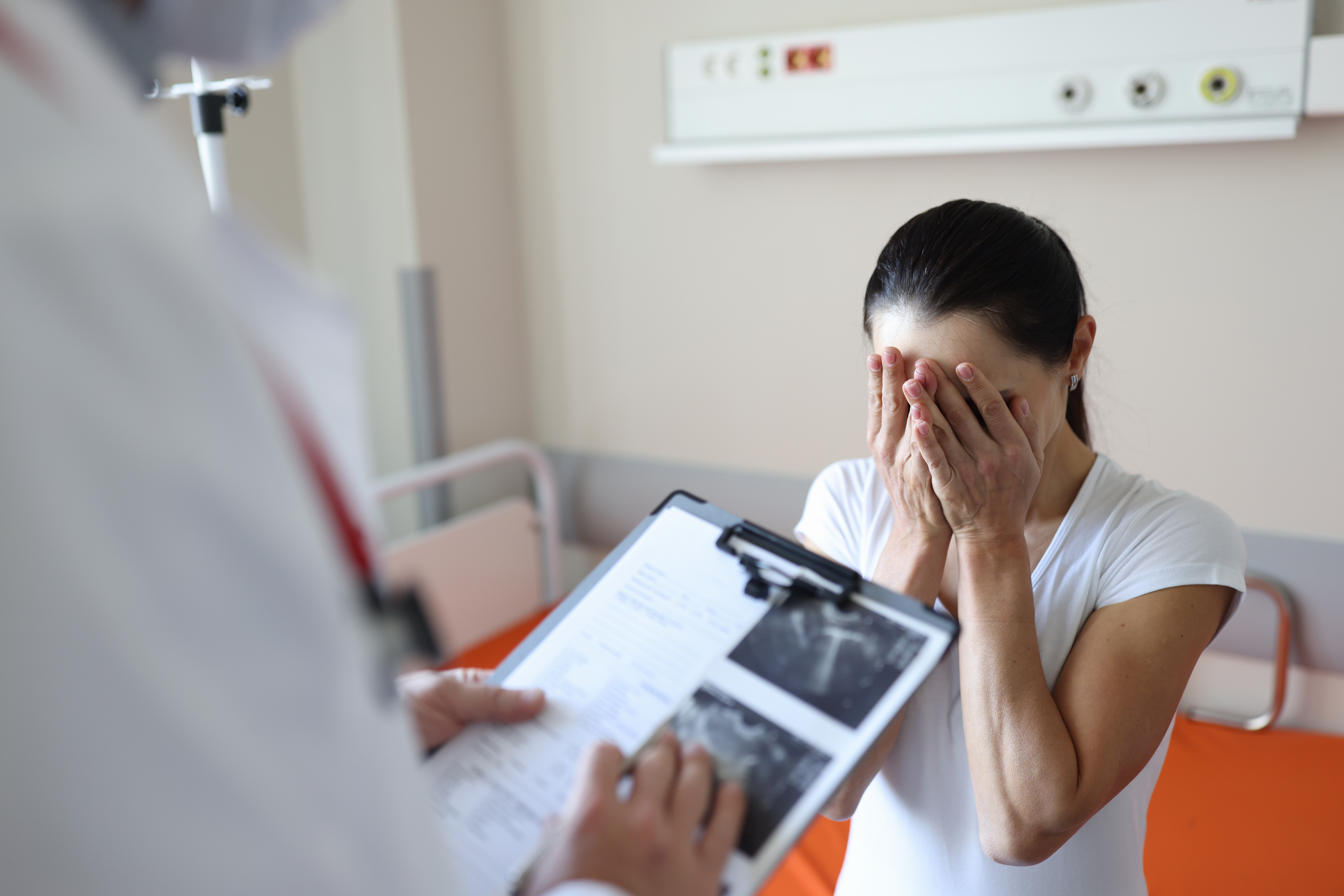 Doctor holding documents in front of crying woman in clinic. | Source: Shutterstock