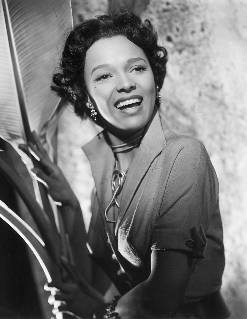 Dorothy Dandridge smiles as she stands next to a large palm frond in a promotional portrait for director Robert Rossen's film, 'Island in the Sun' | Photo: Getty Images