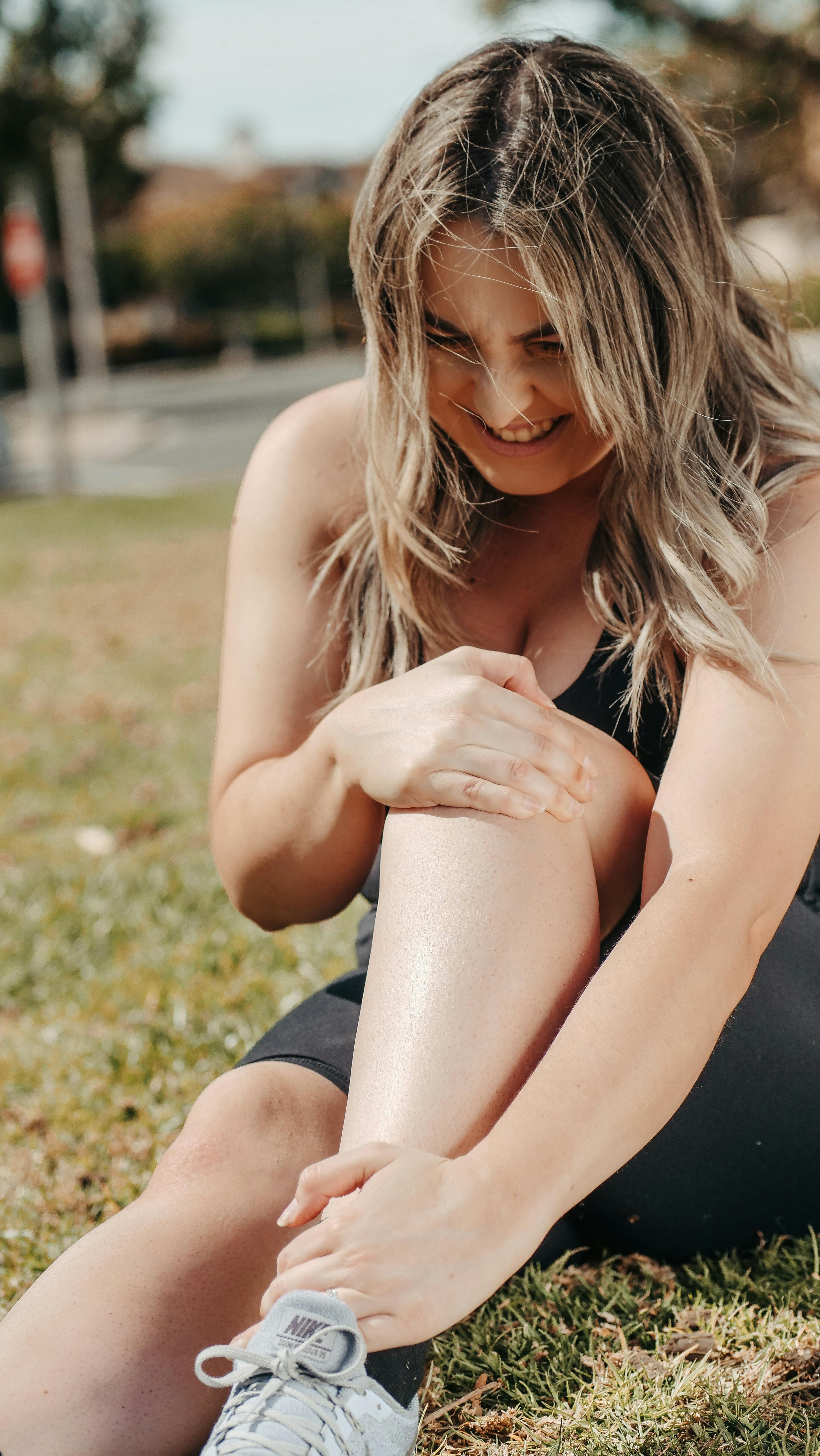 A woman stretching her leg while dealing with workout pain outdoors. | Source: Pexels
