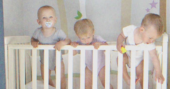 Triplets standing in crib | Shutterstock