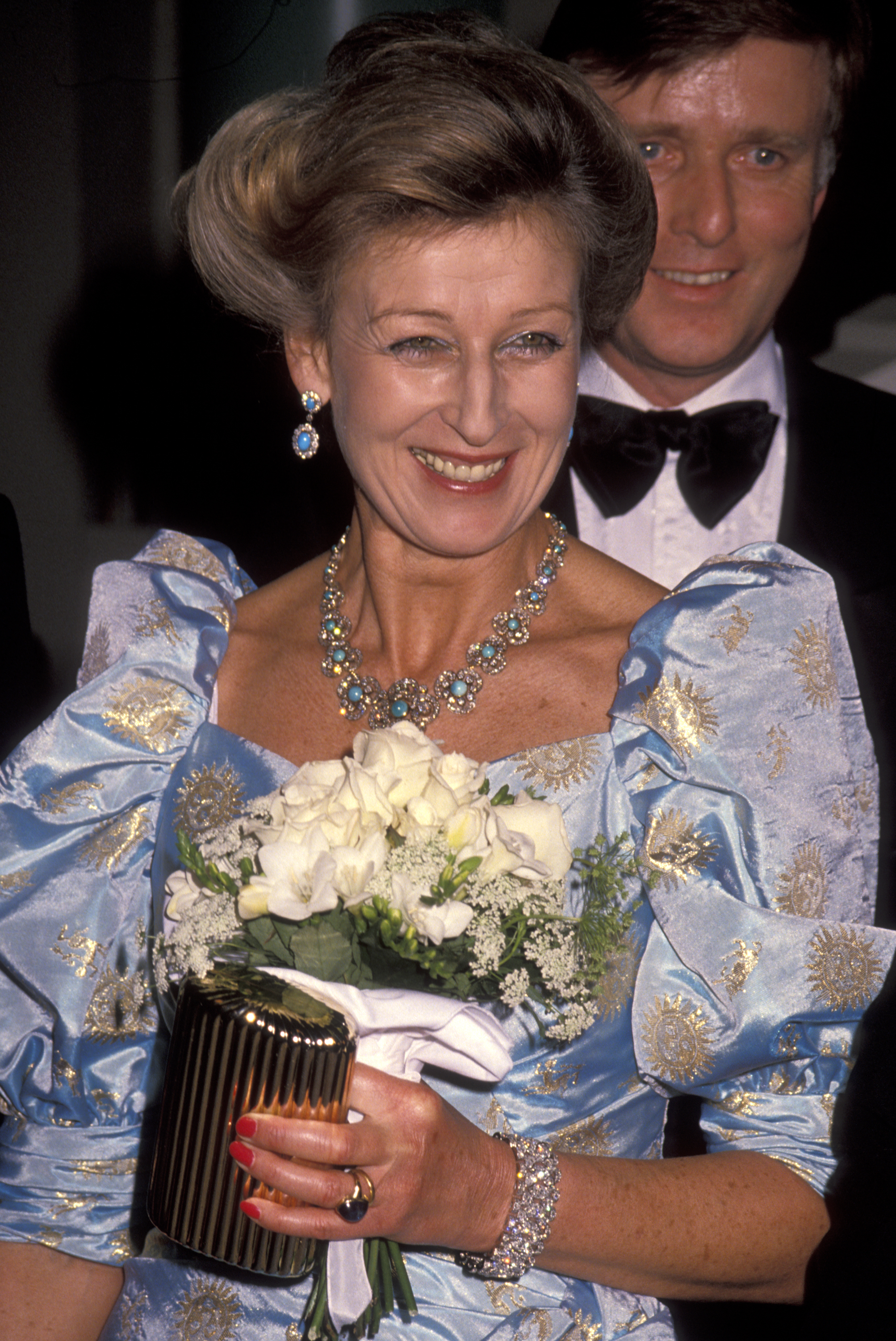 Shining under California lights, Princess Alexandra attends the 1990 BAFTA Gala honouring Sir Michael Caine. Carrying a small bouquet and dressed in a gold-detailed gown, she smiles for cameras — a royal touch of elegance at a star-studded celebration.