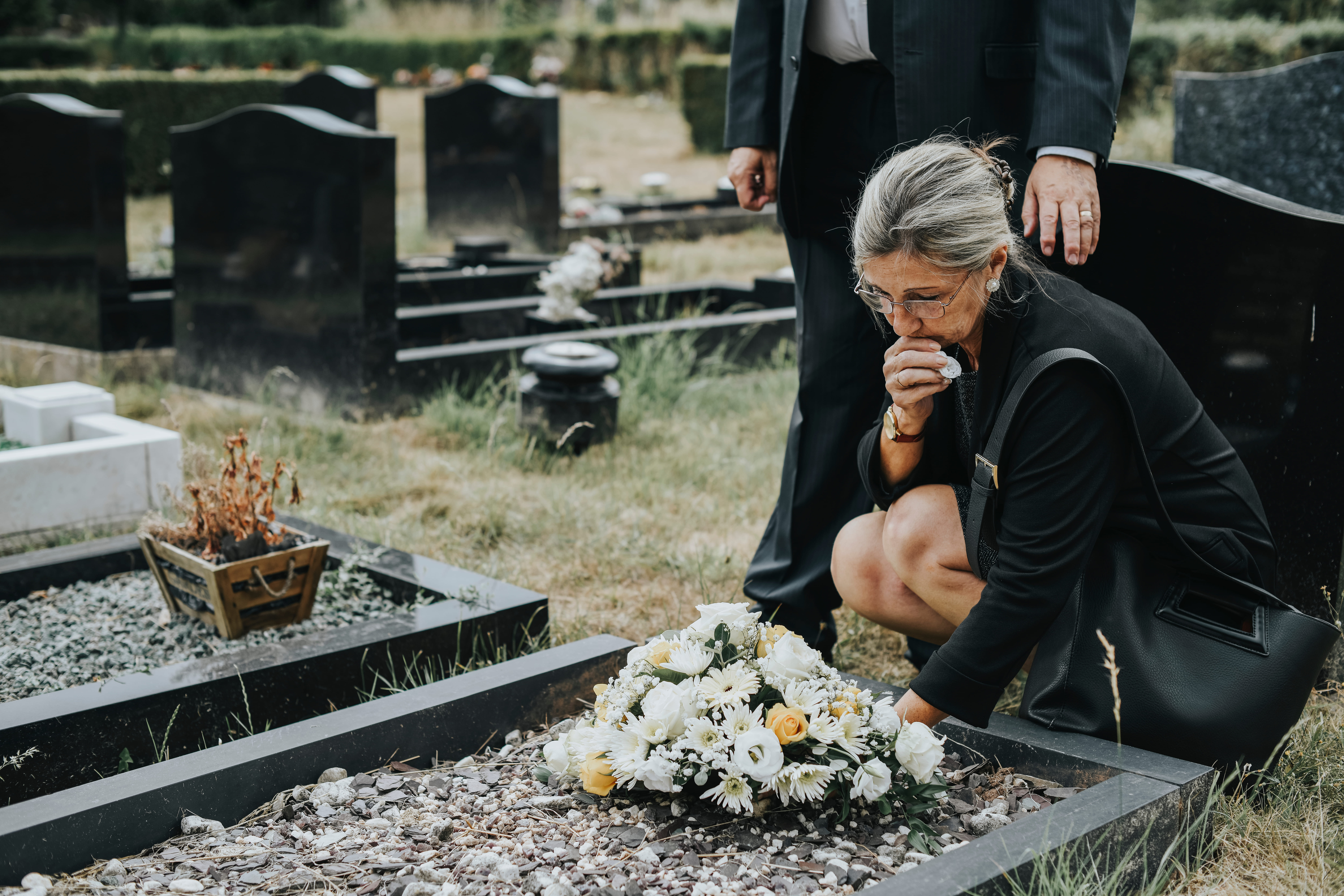 Senior woman placing flowers on a grave | Source: Shutterstock