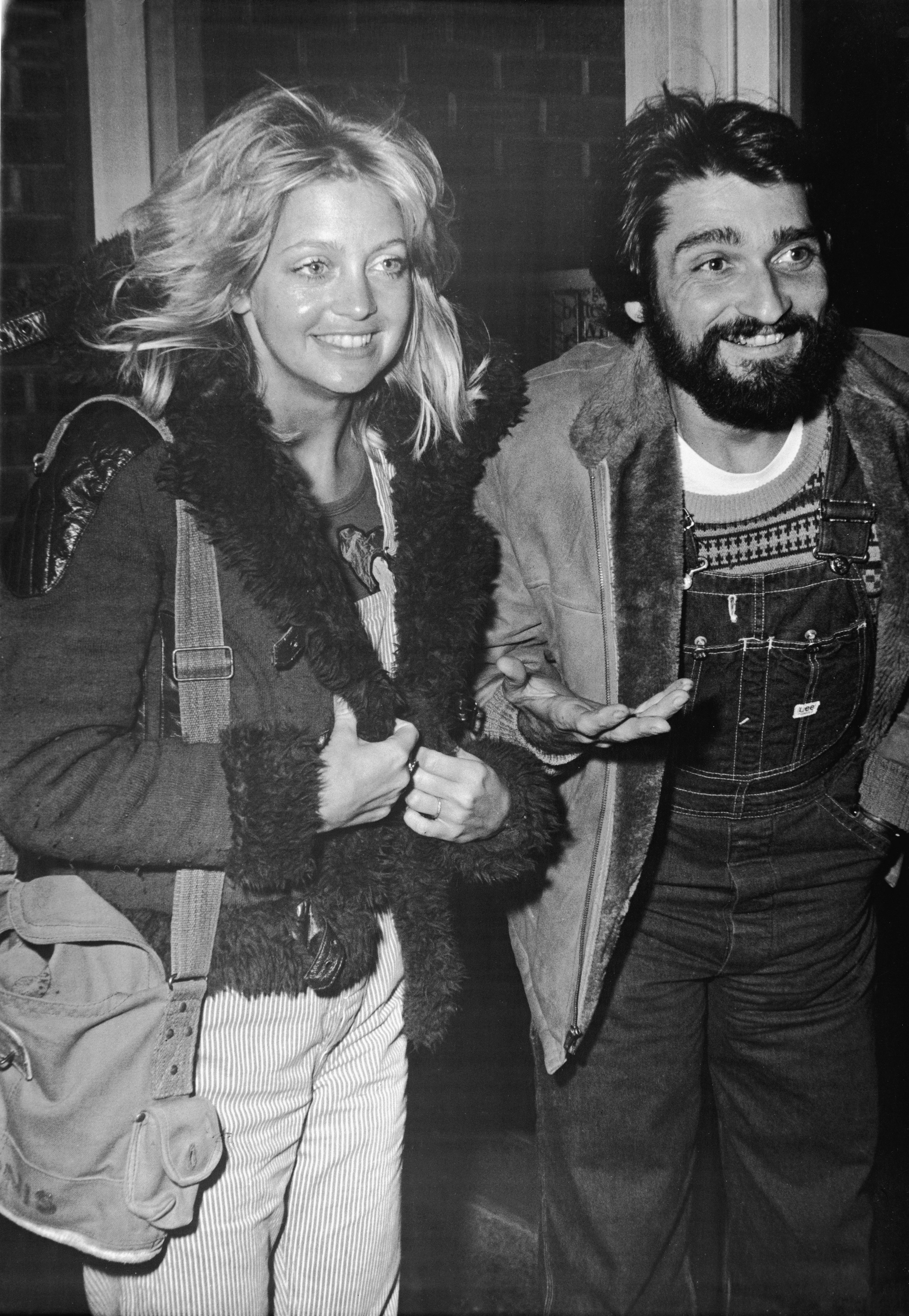 American actress Goldie Hawn and first husband Gus Trikonis stand and smile as they both wear fur-lined jackets and Hudson gestures, late 1970s | Source: Getty Images 