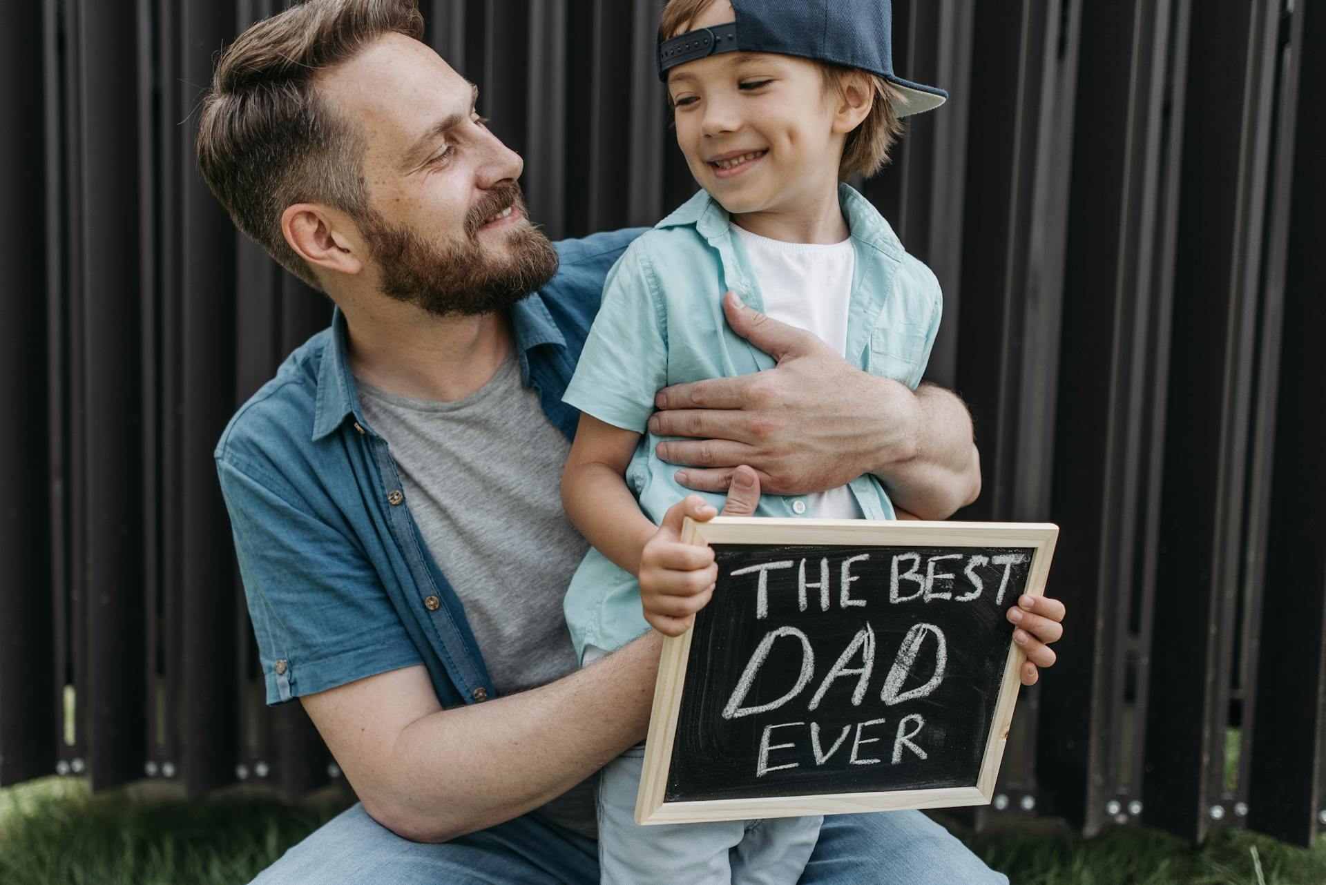 A bearded man embracing his son holding a small blackboard | Source: Pexels