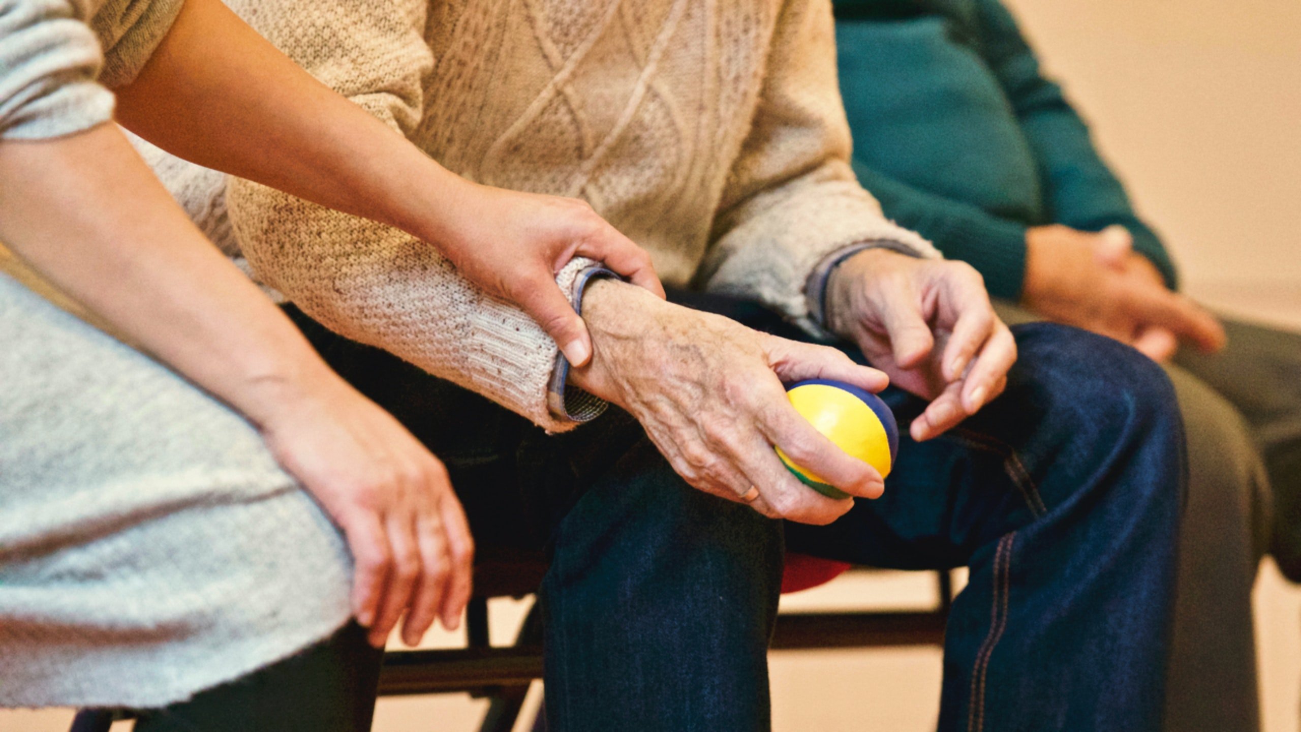 A woman wearing a gray outfit holding the arm of an elderly man who holds a stress ball in his hand | Source: Pexels 