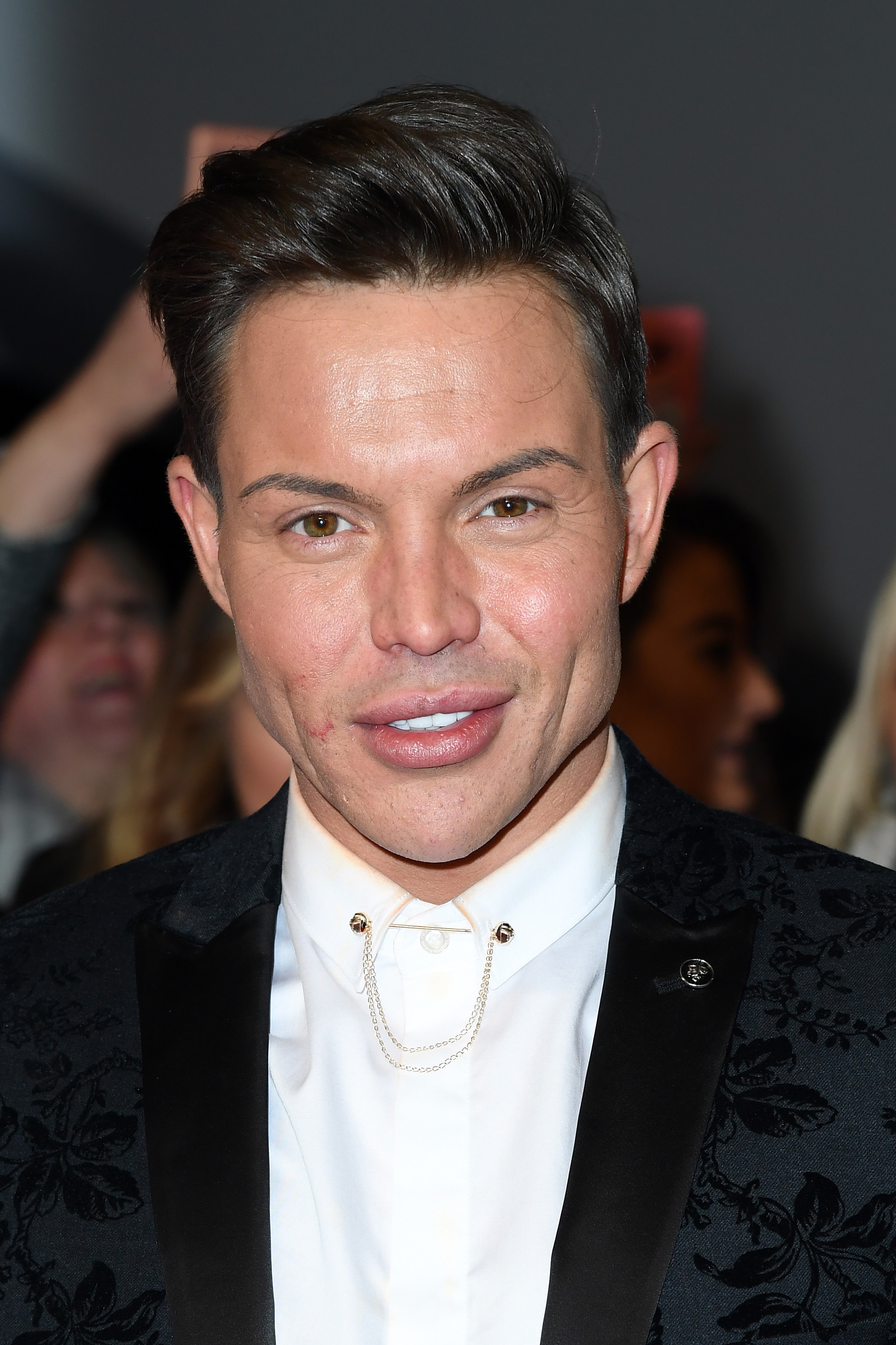 Norris brought some quiet glamour to the National Television Awards in January 2020, wearing a black floral-jacquard blazer fastened with a delicate gold collar chain — a close-up shot that shows his look at its most heavily altered at the time.