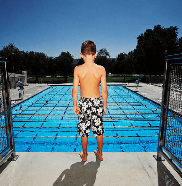Little boy in a swim suit stand's on a diving platform of a community swimming pool | Source: Getty Images