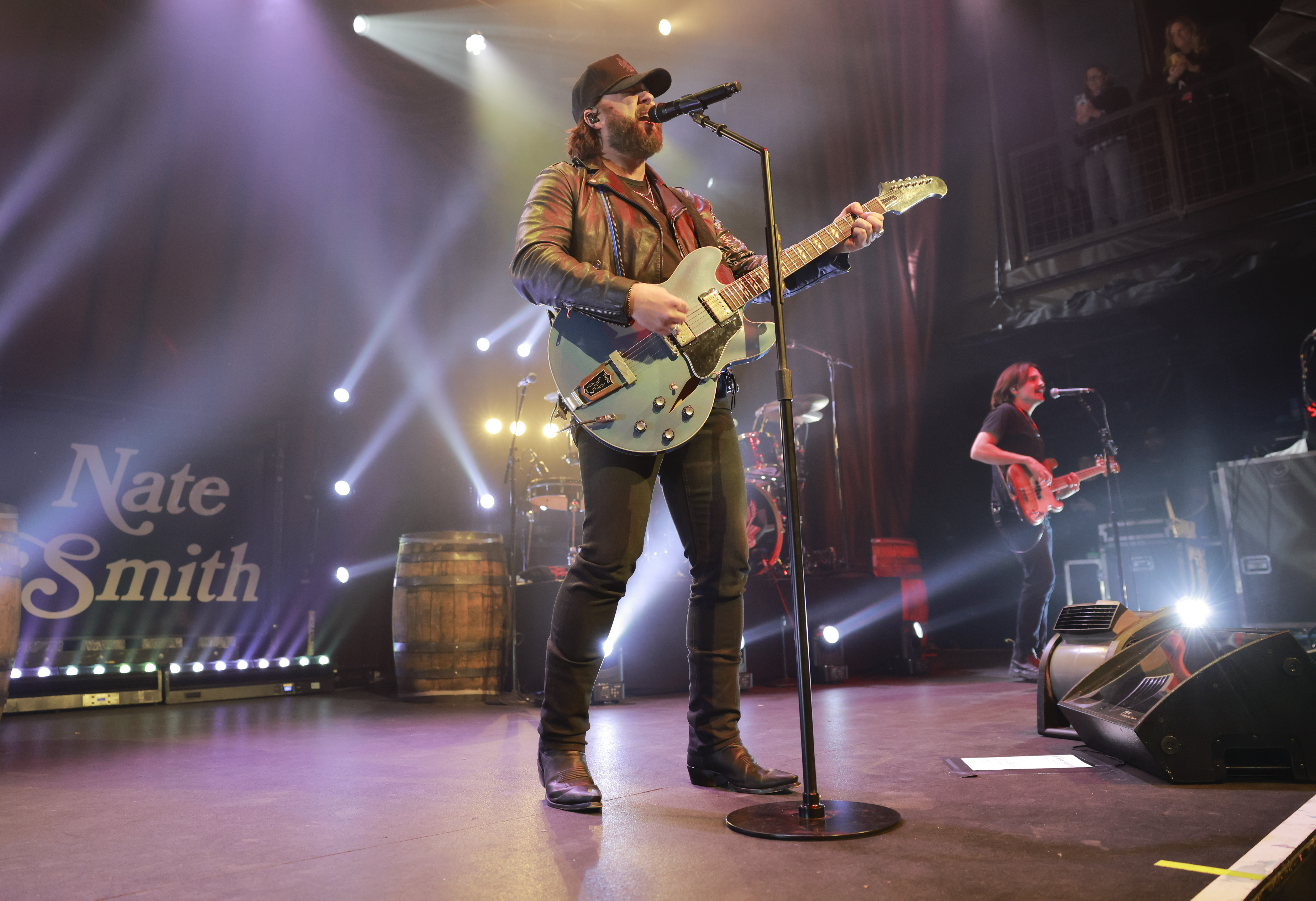 Nate Smith takes command of the stage with an electric guitar in hand, singing beneath sweeping beams of light as his band performs behind him.