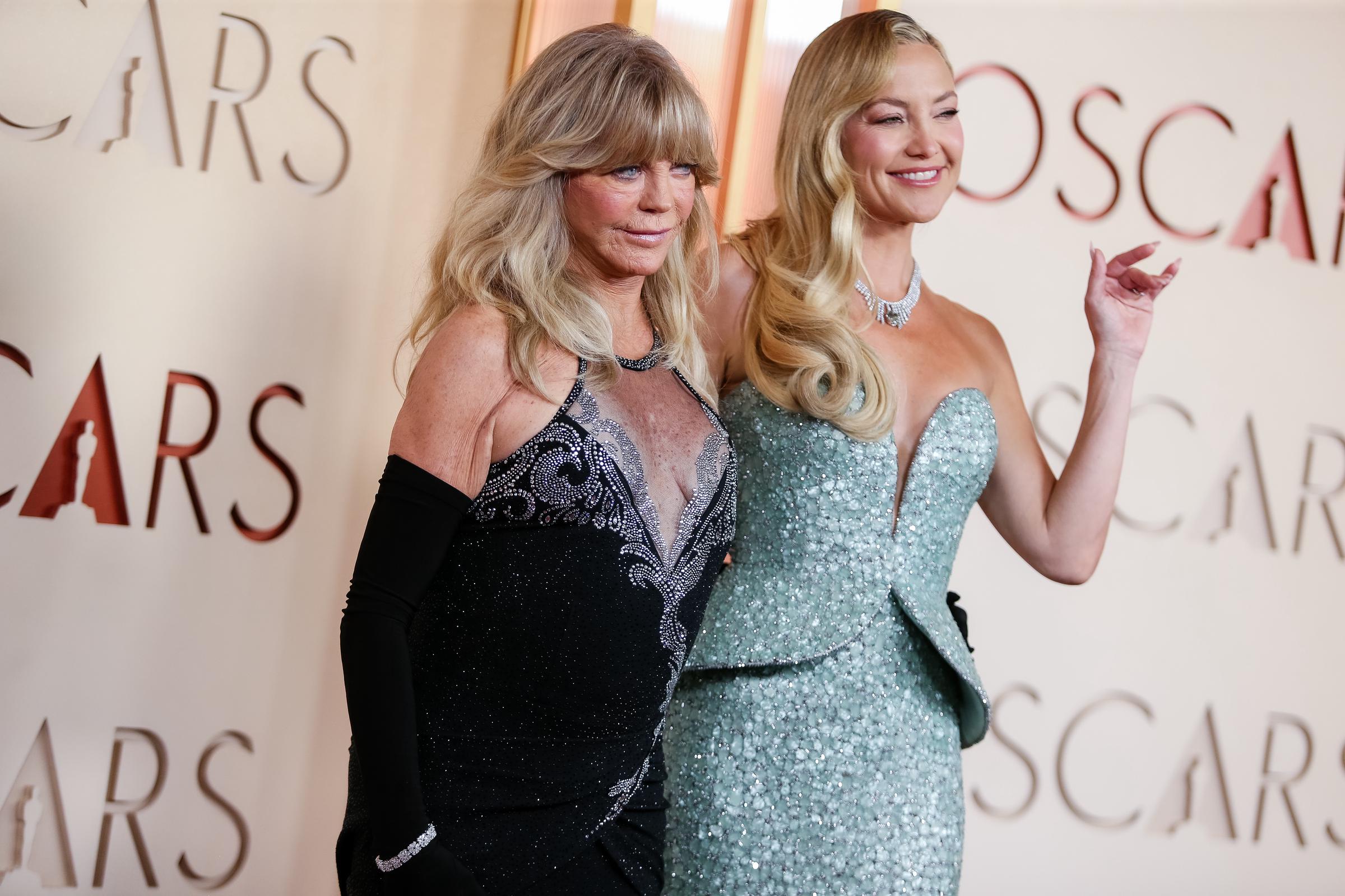 Goldie Hawn and Kate Hudson pose together for photographers, with Hudson smiling and gesturing toward the crowd as they stand side by side on the red carpet.