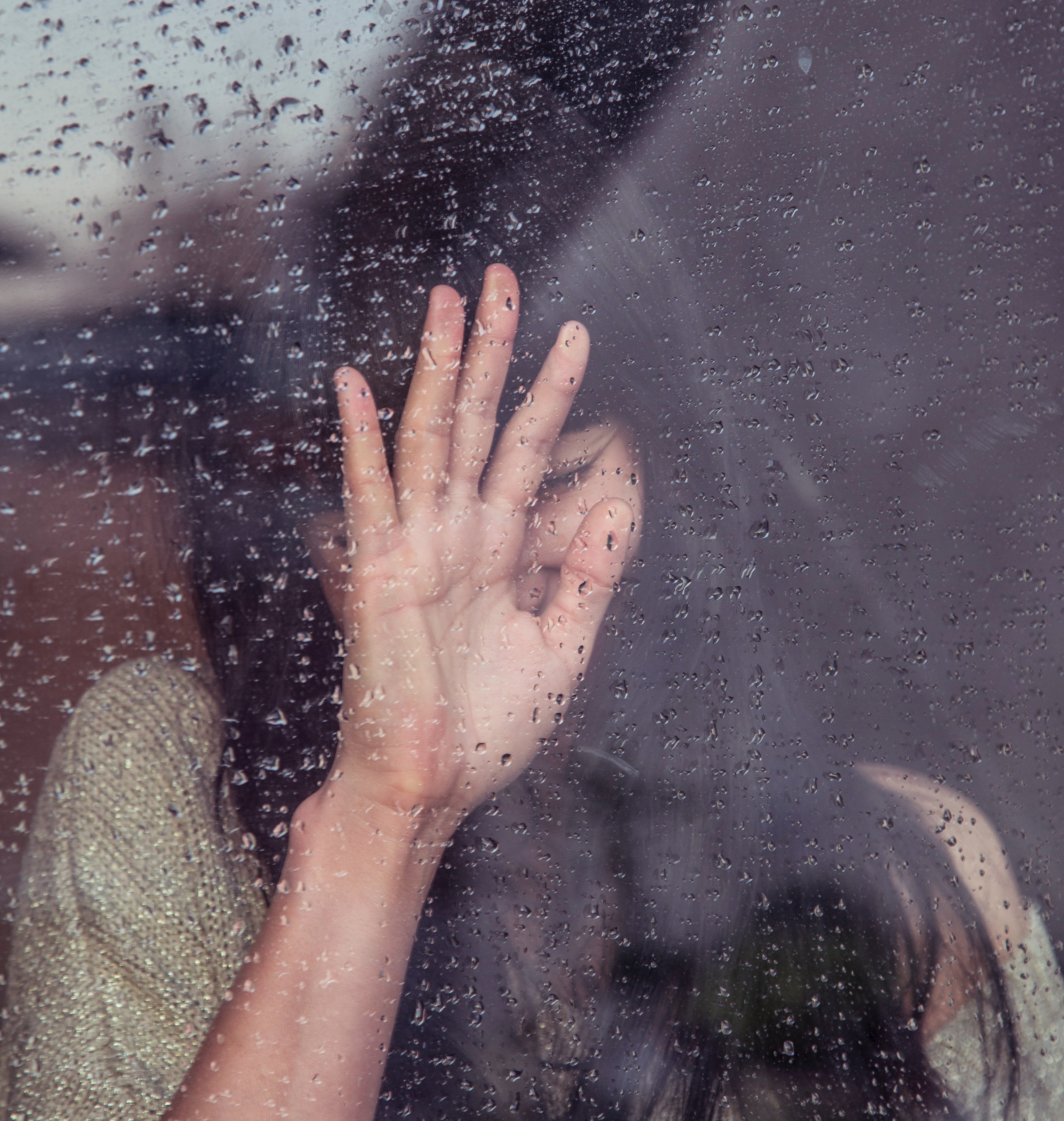 Una mujer joven llora frente a una ventana un día de lluvia. | Foto: Unsplash