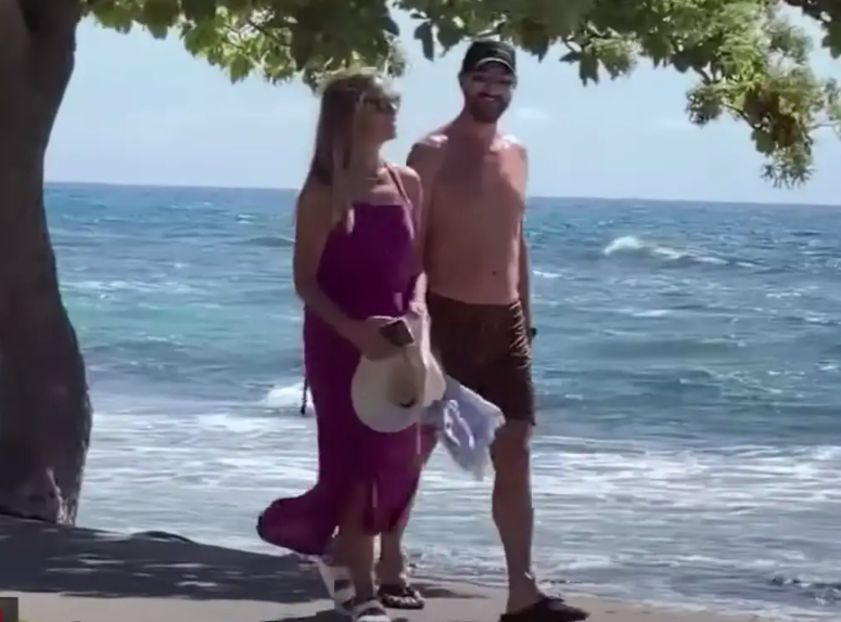 A screenshot from a YouTube video of Christine Baumgartner and Josh Connor walking along the beach in Hawaii posted on July 24, 2023 | Source: YouTube/TMZ