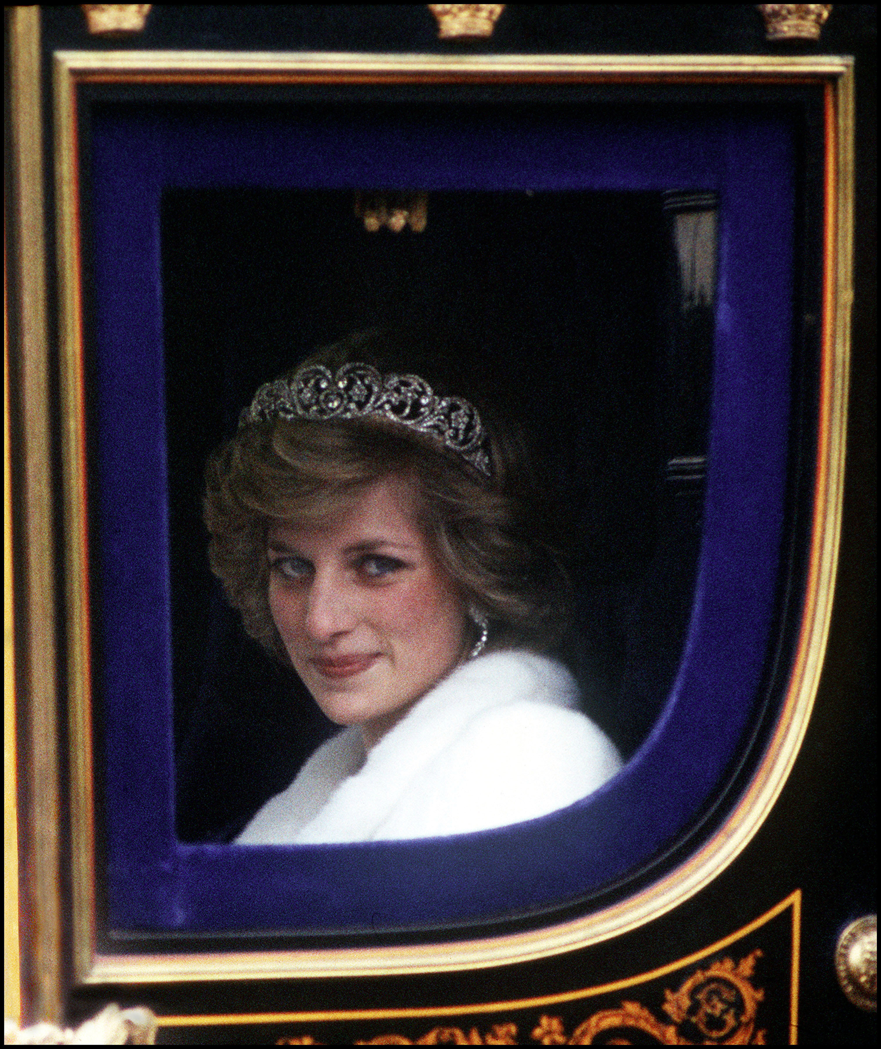 Princess Diana, radiant in a white fur coat and the famed Spencer tiara, rides in regal splendor to the State Opening of Parliament in November 1982. The young Princess of Wales joins Queen Elizabeth II in one of her earliest ceremonial roles as a senior royal.
