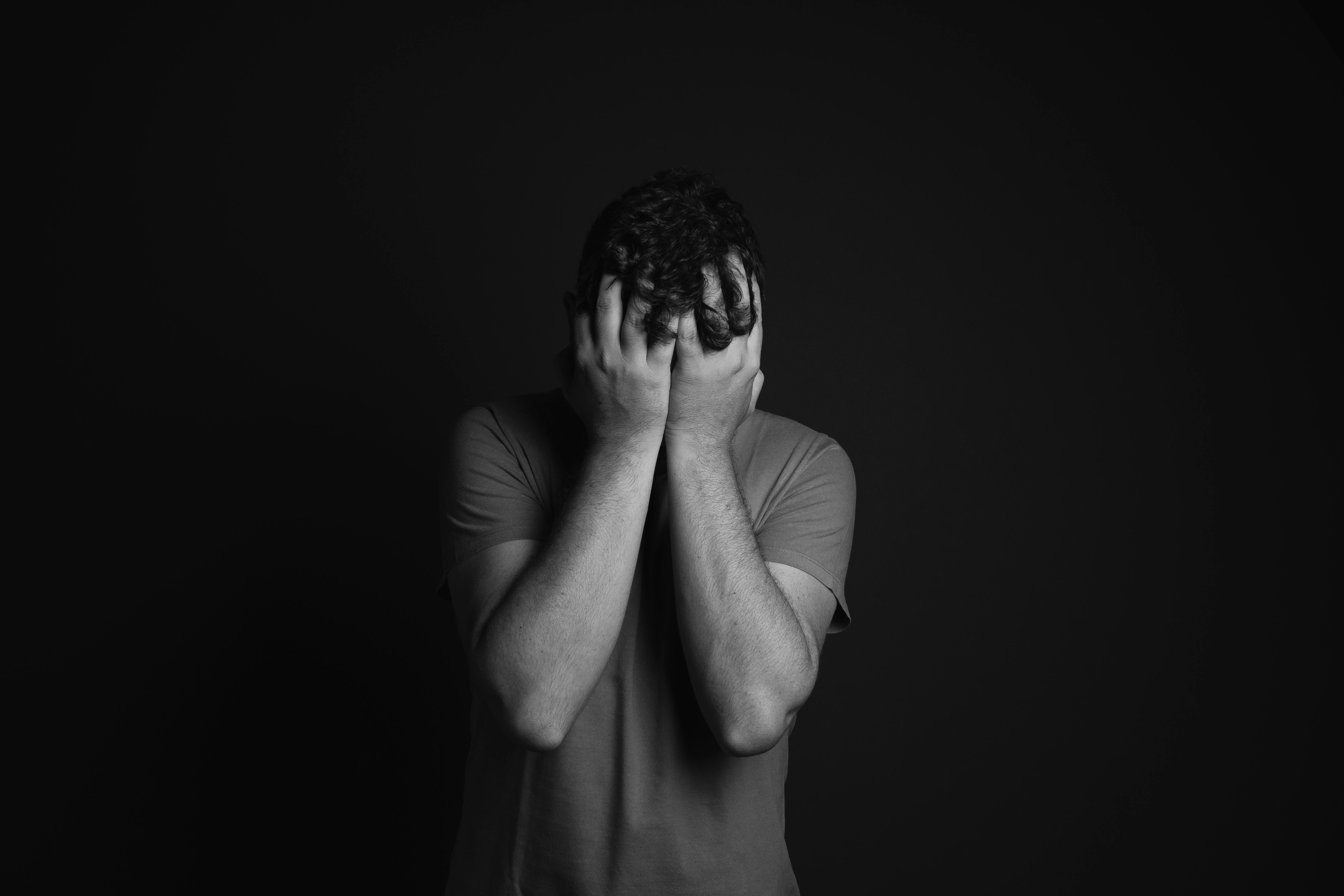 Grayscale photo of a man covering his face with his hands | Source: Pexels