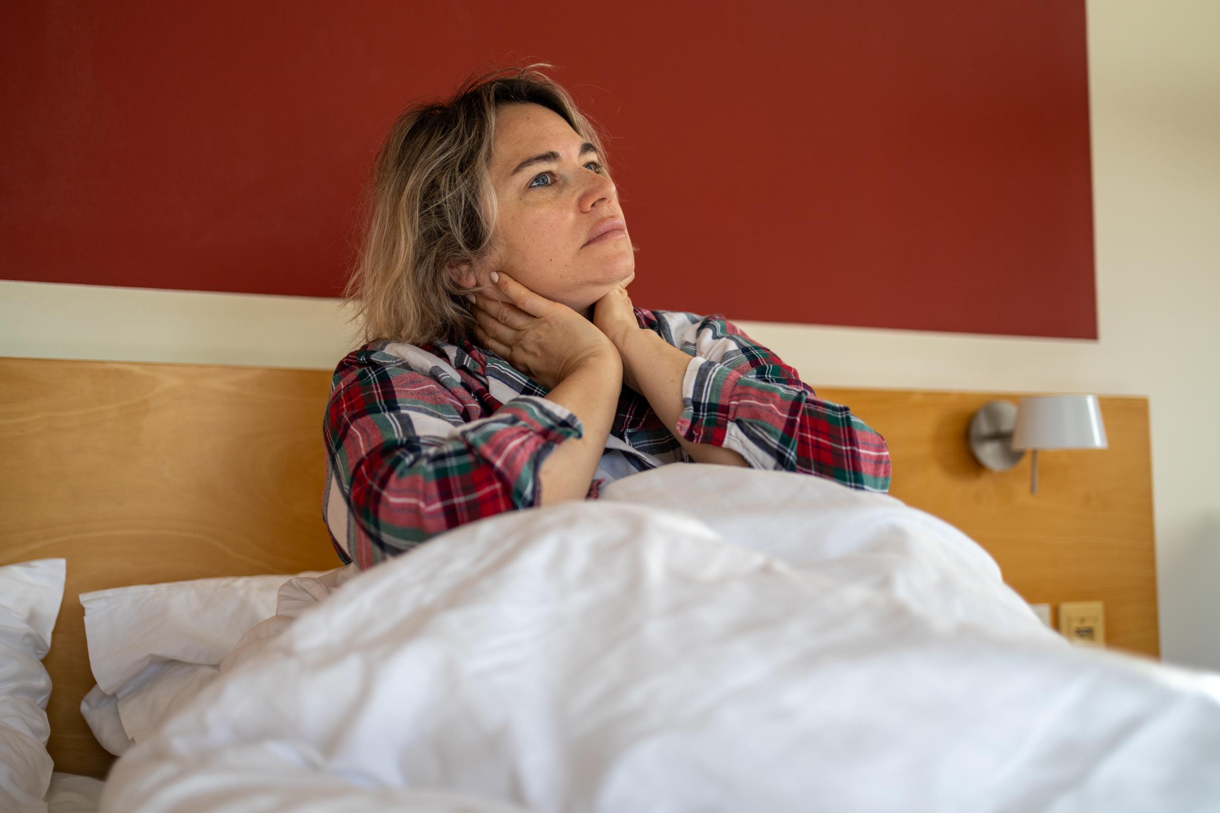 Tired woman sitting in bed, holding her neck in pain, symbolizing stress, burnout, and mental health struggles | Source: Getty Images