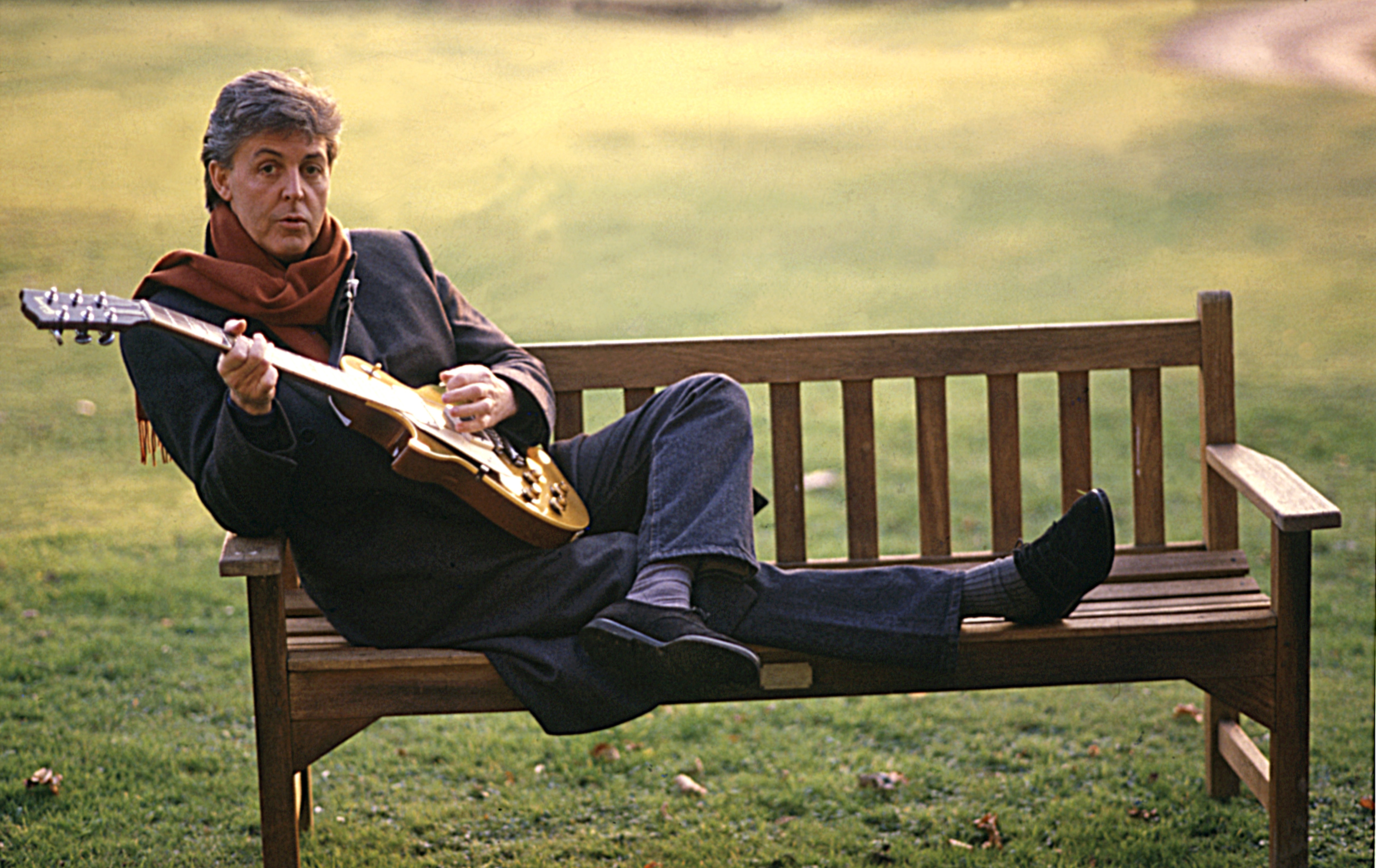 Paul McCartney sitting on a bench and playing a Gibson Les Paul guitar in 1987. | Source: Getty Images