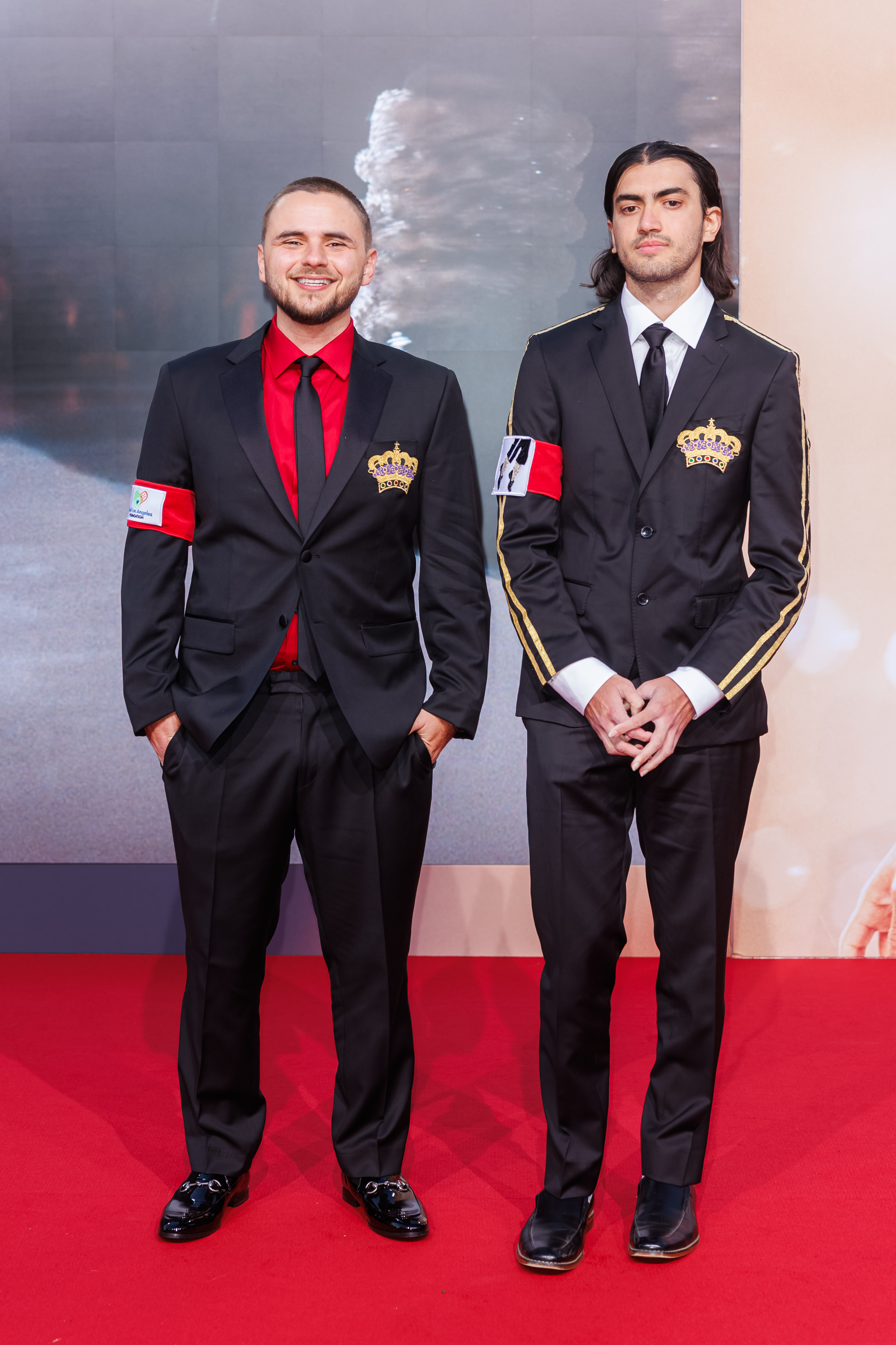 Prince Jackson and Bigi Jackson wear black single-breasted suits featuring gold crown decals and armbands displaying Michael Jackson's feet in an iconic dance move.