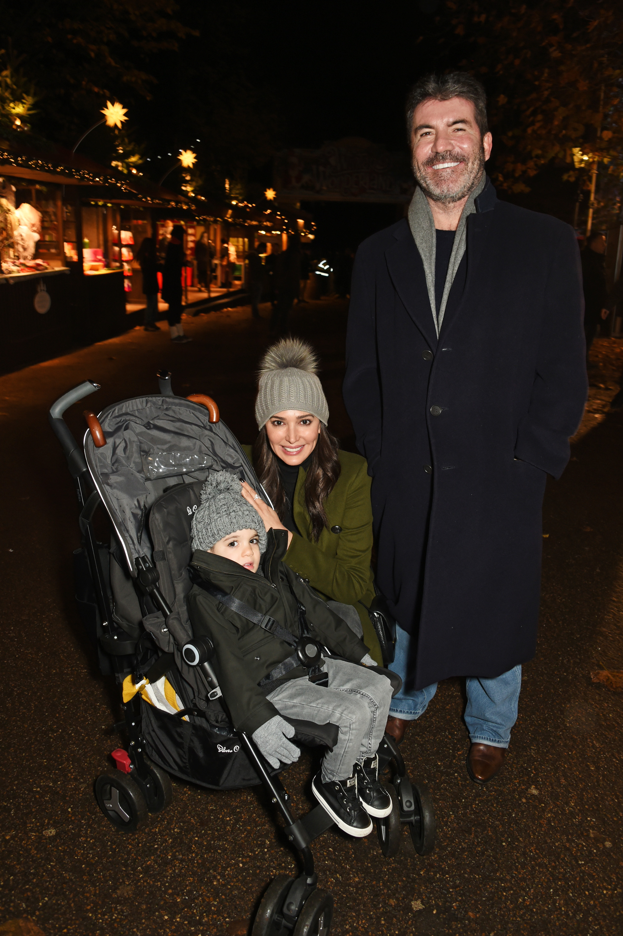 Simon Cowell, alongside Lauren Silverman and Eric, attended a VIP Preview of Hyde Park's Winter Wonderland in London, United Kingdom. Cowell stands tall with his hands in his pockets, while Silverman crouches beside a stroller to pose with their toddler.