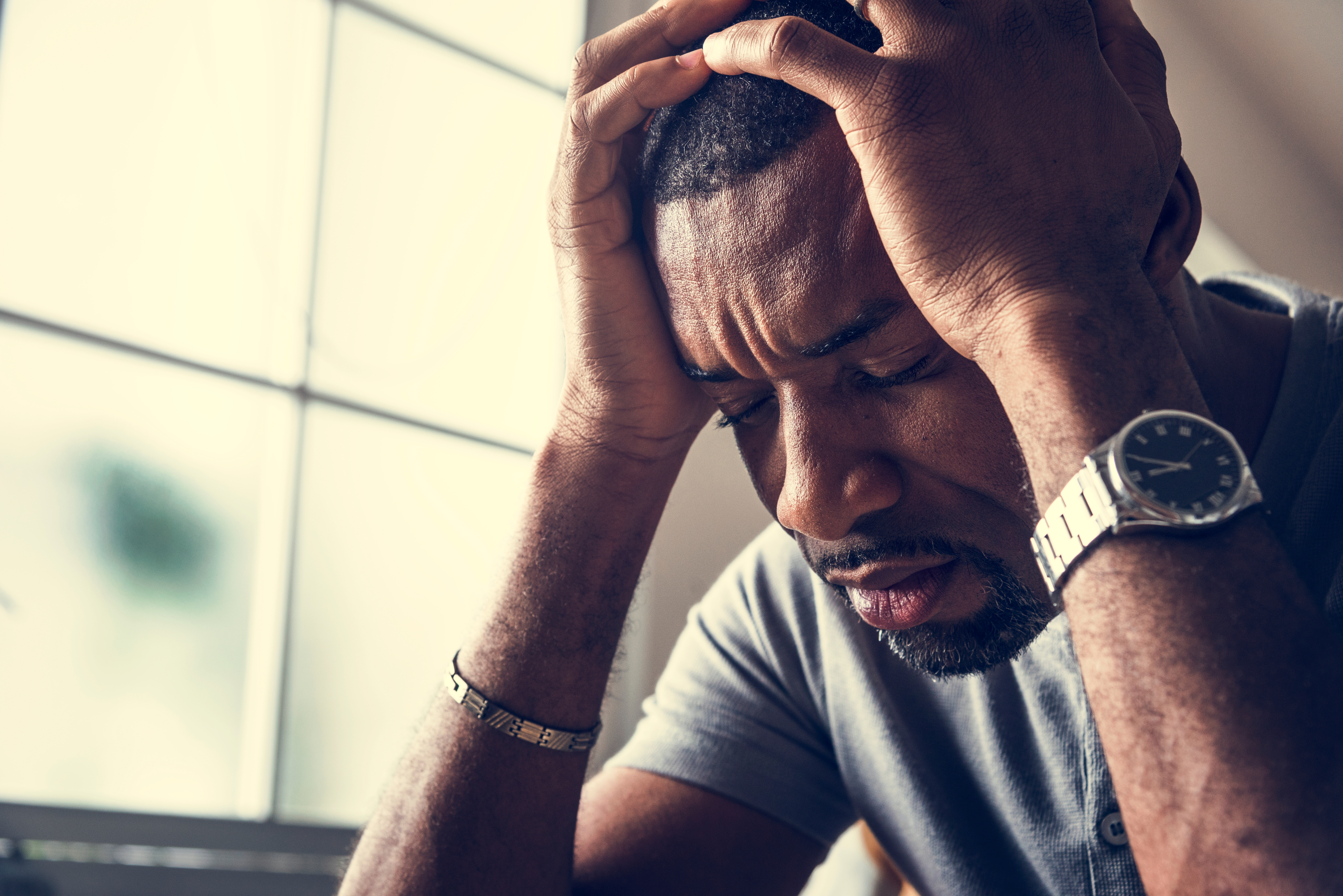 A stressed-out black man sits holding his head in his hands | Source: Shutterstock