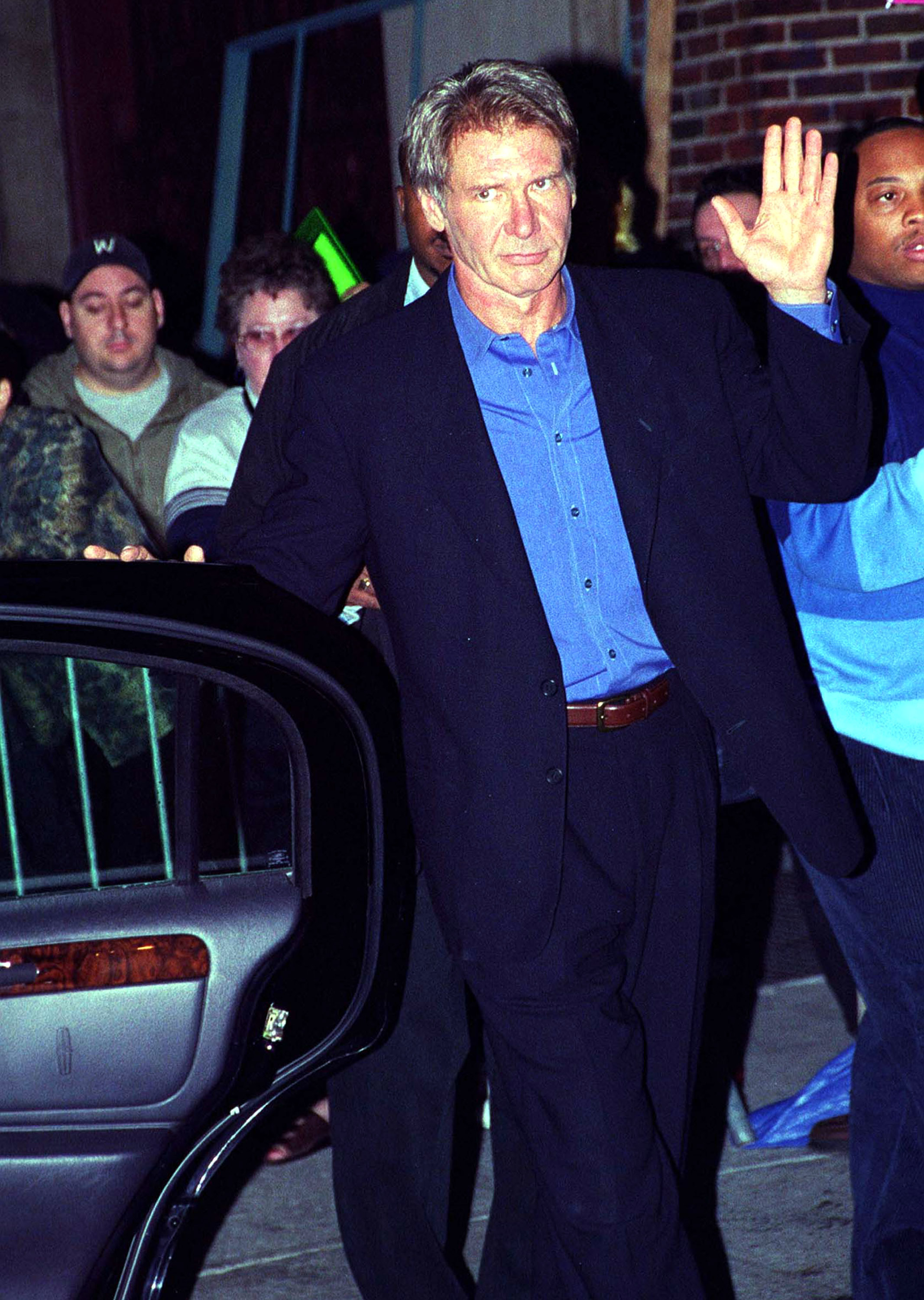 Waving to a crowd of eager fans, Ford looks incredibly sharp as he leaves "The Late Show with David Letterman" in New York City. Dressed in a tailored dark blazer and a vibrant blue button-down shirt, the actor shows off the trim, active frame that has kept him in action-hero shape for decades. | Source: Getty Images