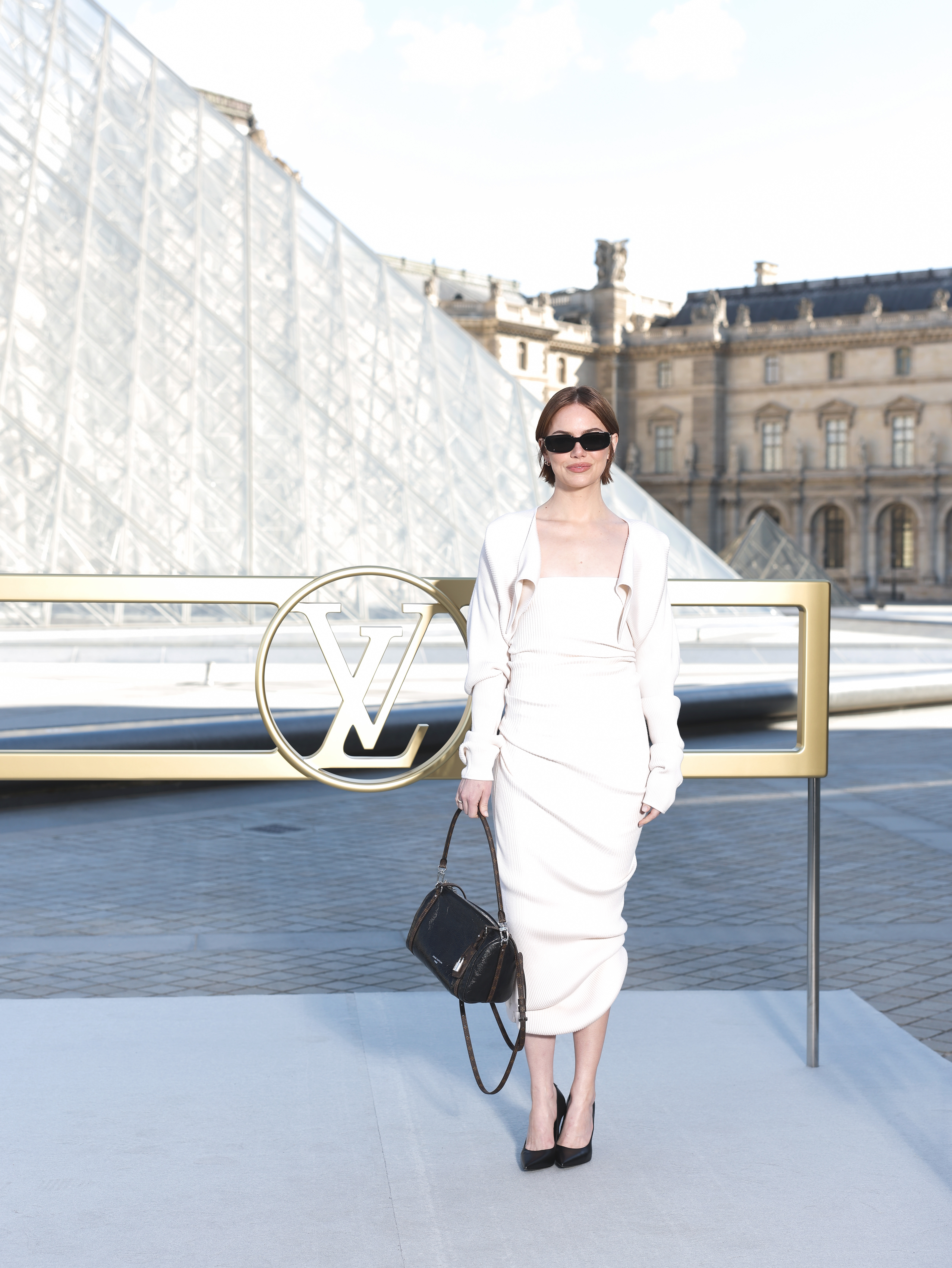 Emma Stone attended the Louis Vuitton Women’s Spring/Summer 2026 show at Paris Fashion Week in France. She wore a creamy white, heavily ribbed midi-length dress that showcased texture and silhouette mastery. It was paired with sharp black accessories to anchor the monochromatic look.