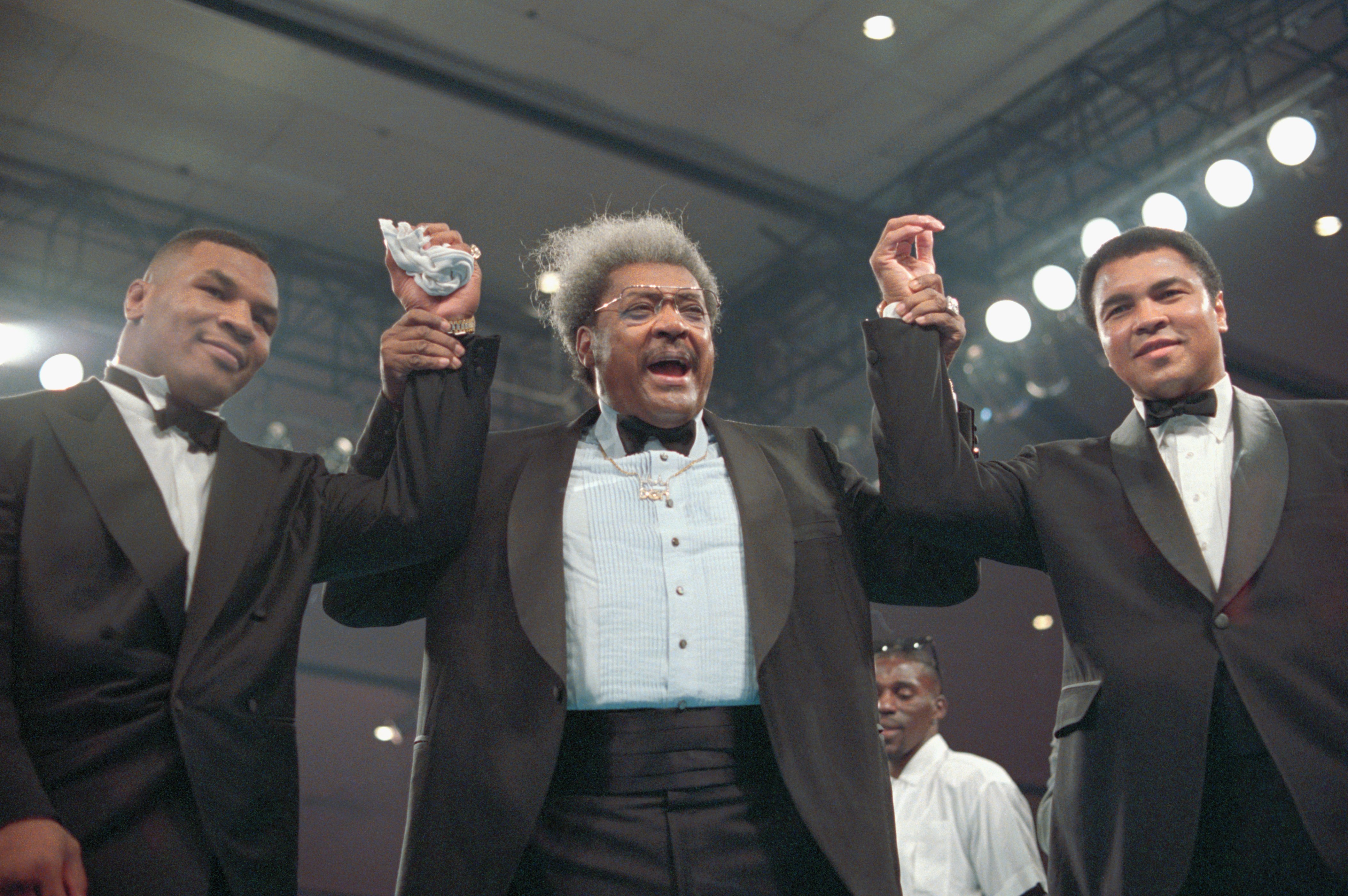 Mike Tyson, Don King, and Mohammed Ali, all clasping hands wearing tuxedos in the boxing ring at the Las Vegas Hilton | Source: Getty Images