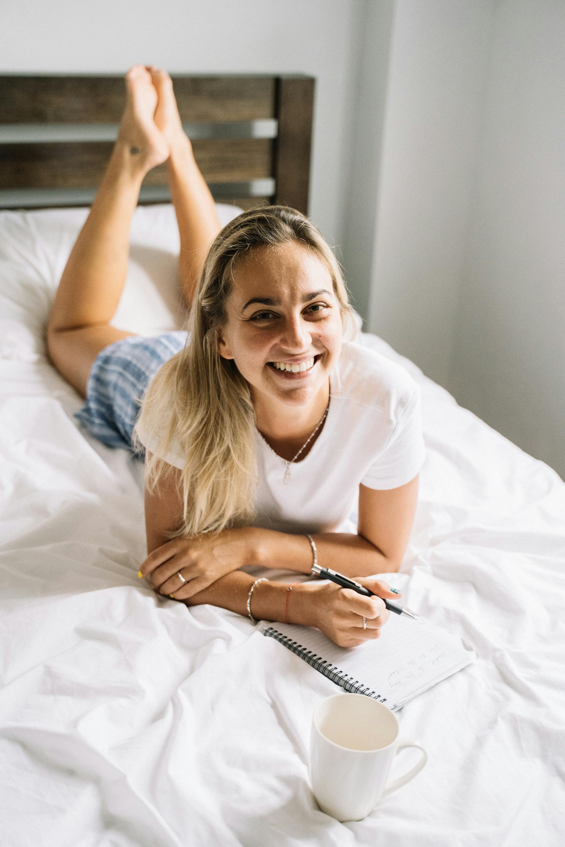 A woman lying on her bed holding a pen and notebook | Source: Pexels