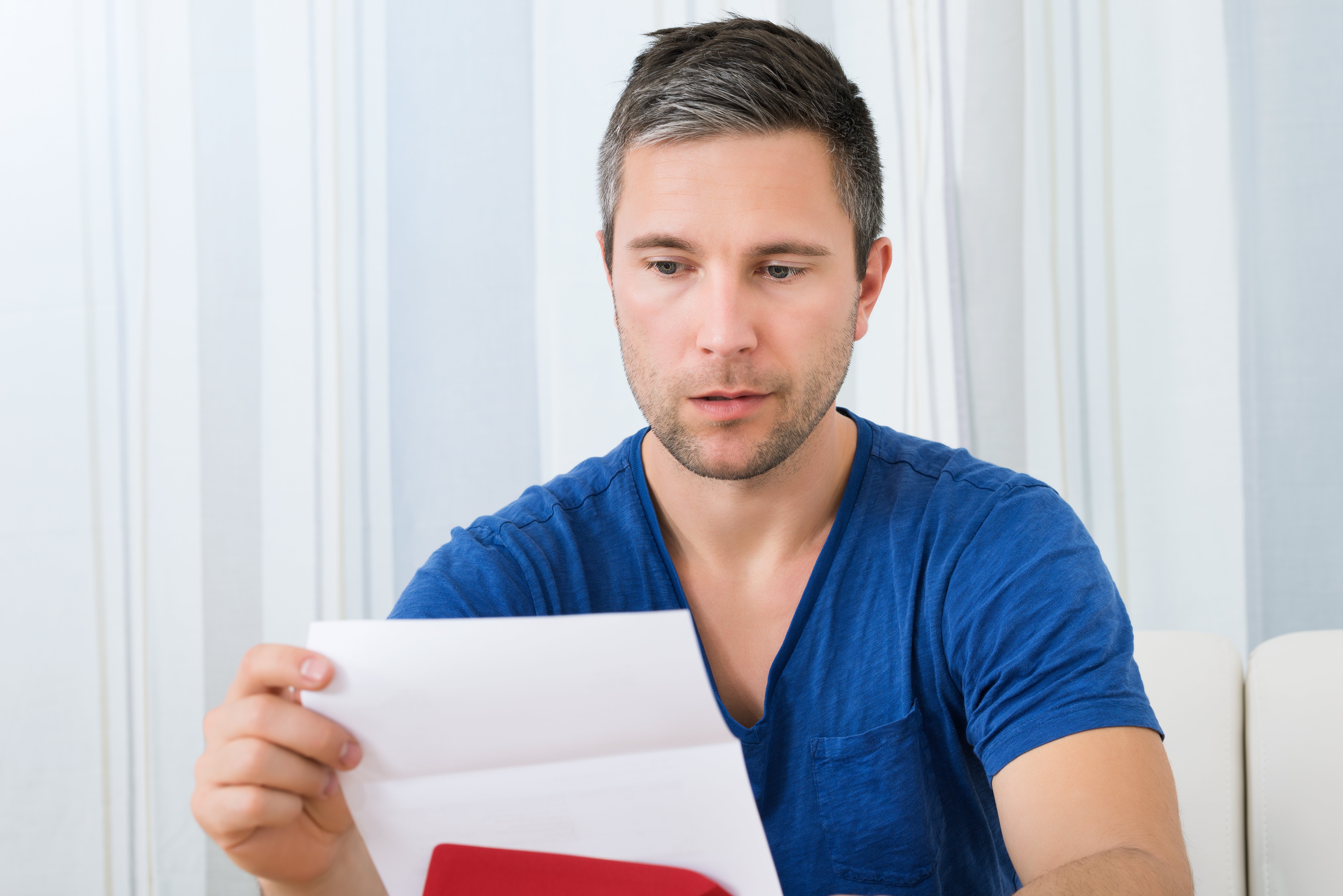 Portrait Of Unhappy Man Sitting On Sofa Reading A Piece of Paper | Photo: Shutterstock.com