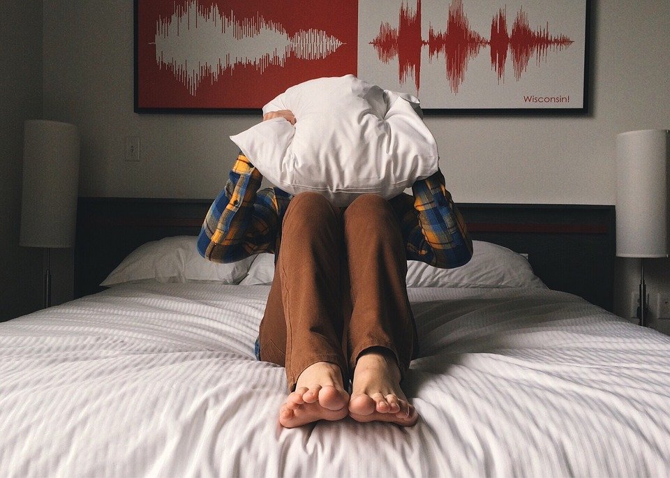 Joven sentado en la cama se tapa la cara con la almohada. | Foto: Pixabay