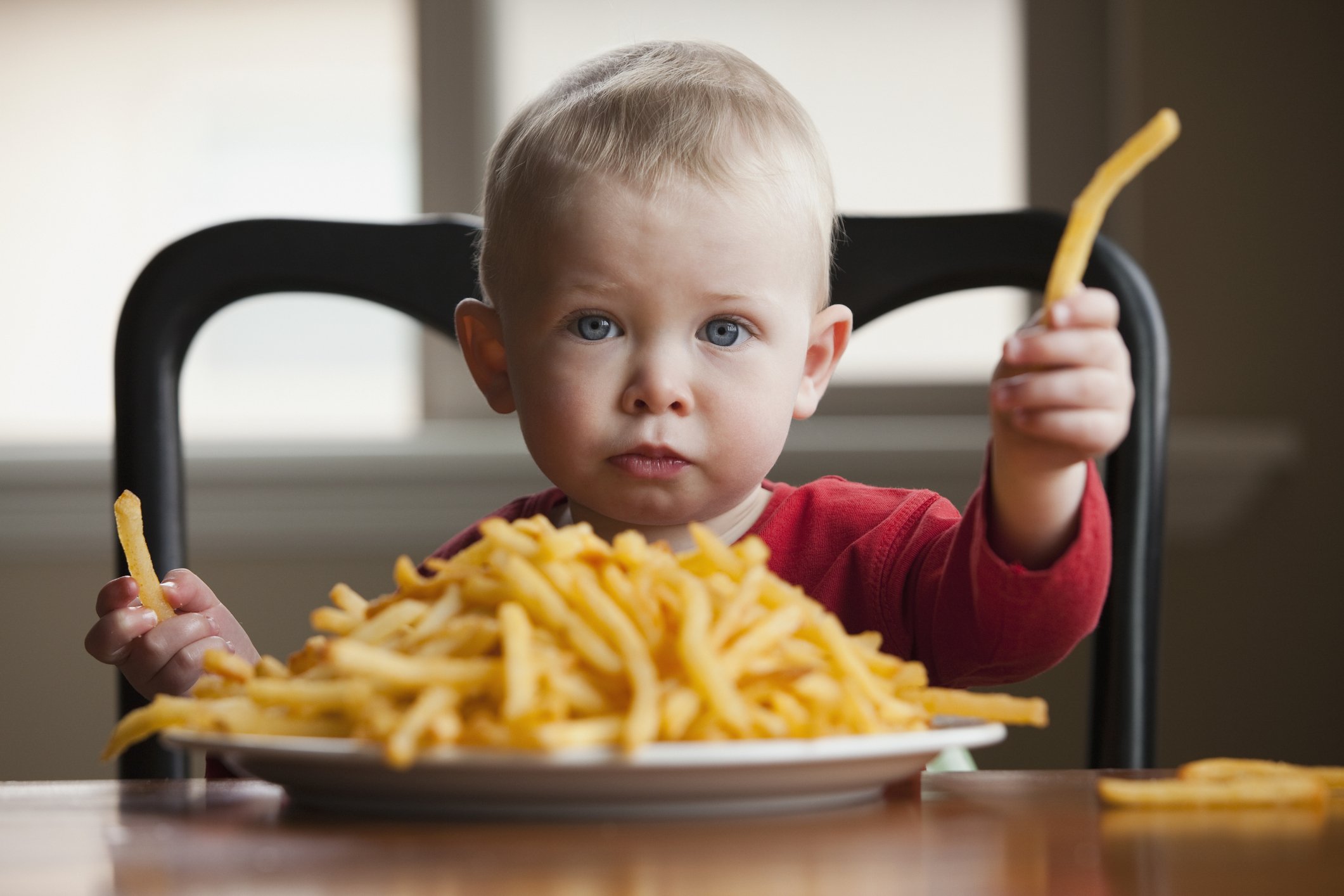 Kleinkind, das einen großen Teller Pommes frites isst | Quelle: Shutterstock