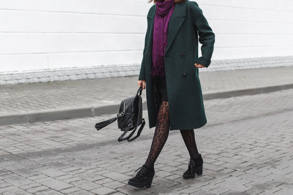 Chica con un abrigo usando una falta y medias estampadas transparentes de color negro. | Foto: Shutterstock