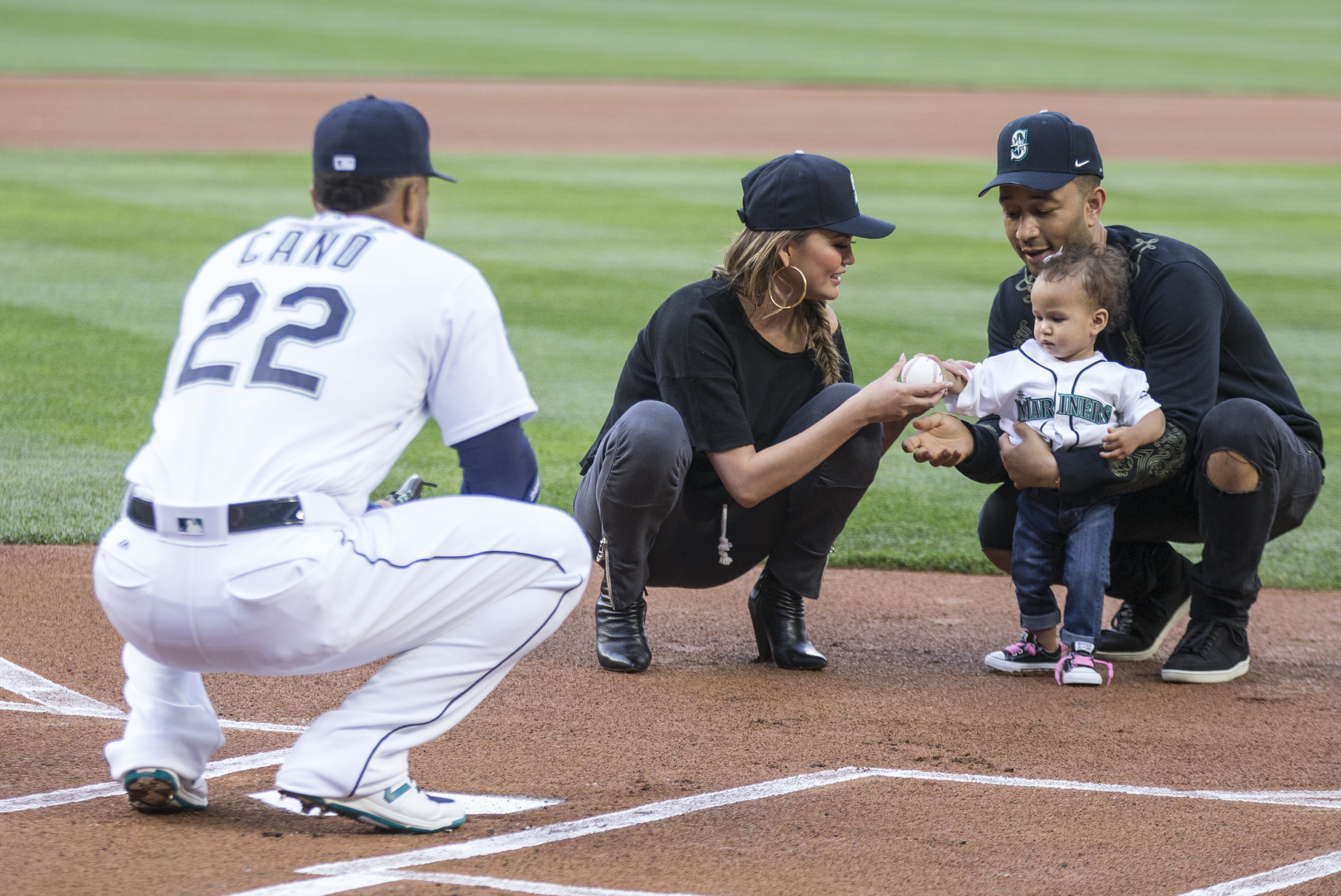 Chrissy Teigen and John Legend help Luna Stephens throw out the ceremonial first pitch to Robinson Cano of the Seattle Mariners before a game | Source: Getty Images