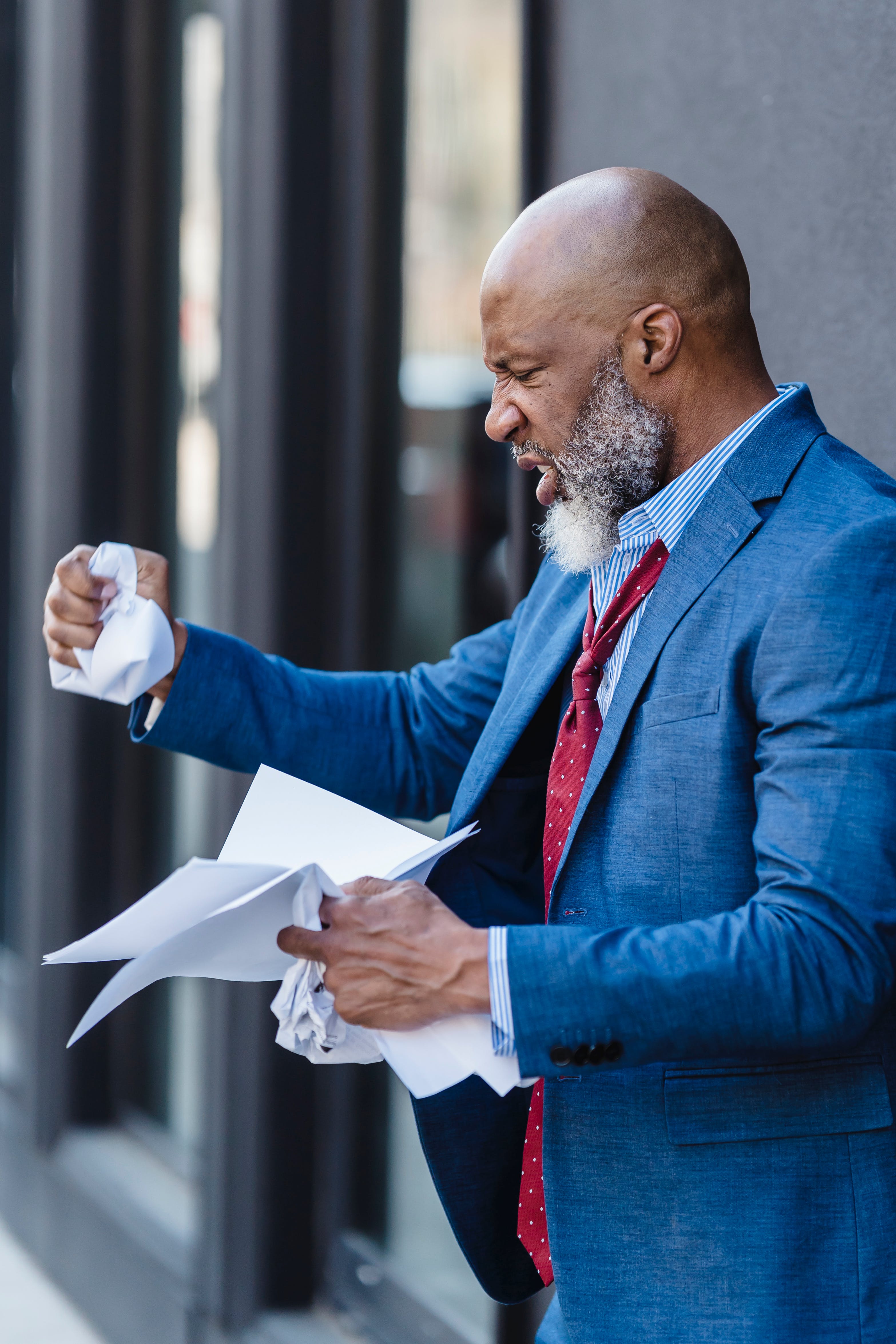 An angry man standing outside crumpling papers in his hand | Source: Pexels