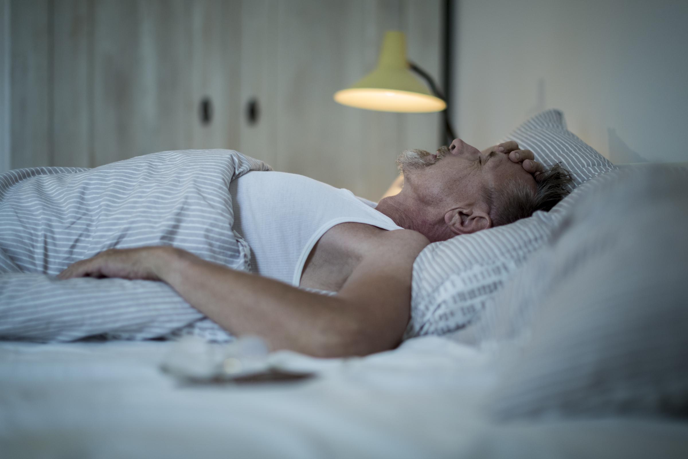 Man lying awake in bed at night, feeling unwell and unable to sleep | Source: Getty Images