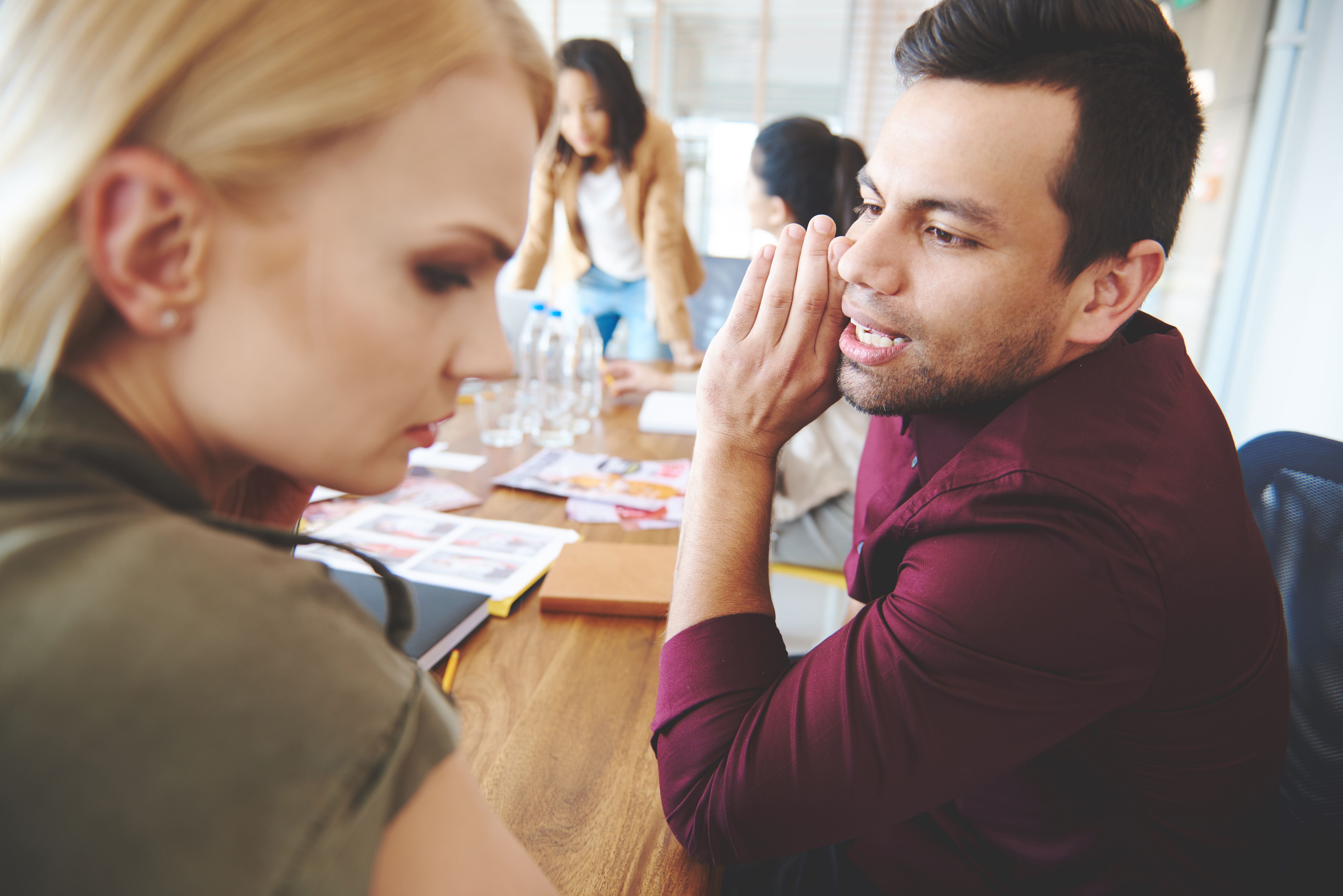 Co-workers whispering during a meeting at work. | Source: Shutterstock