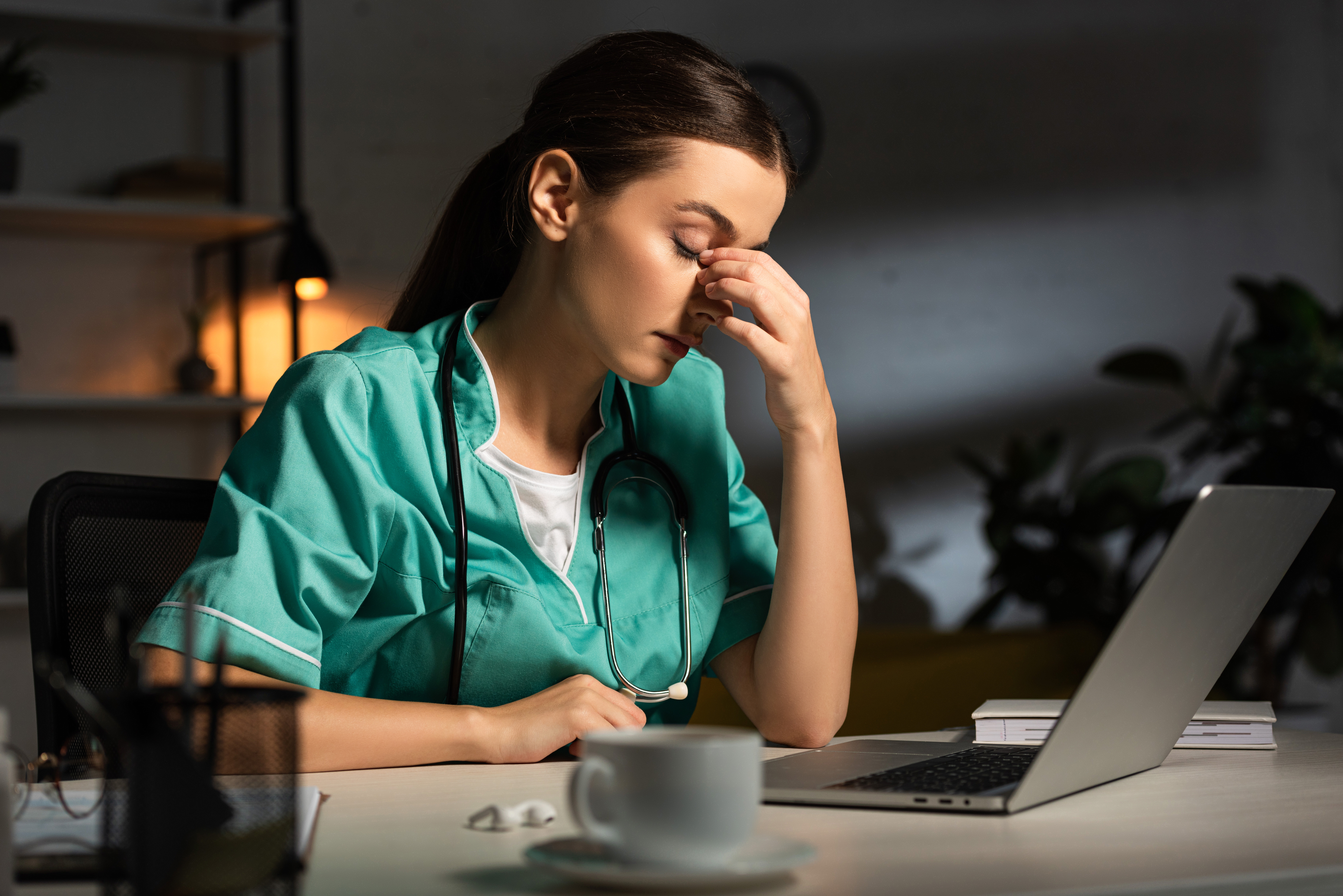 Tired nurse in uniform sitting at table during night shift | Source: Shutterstock.com