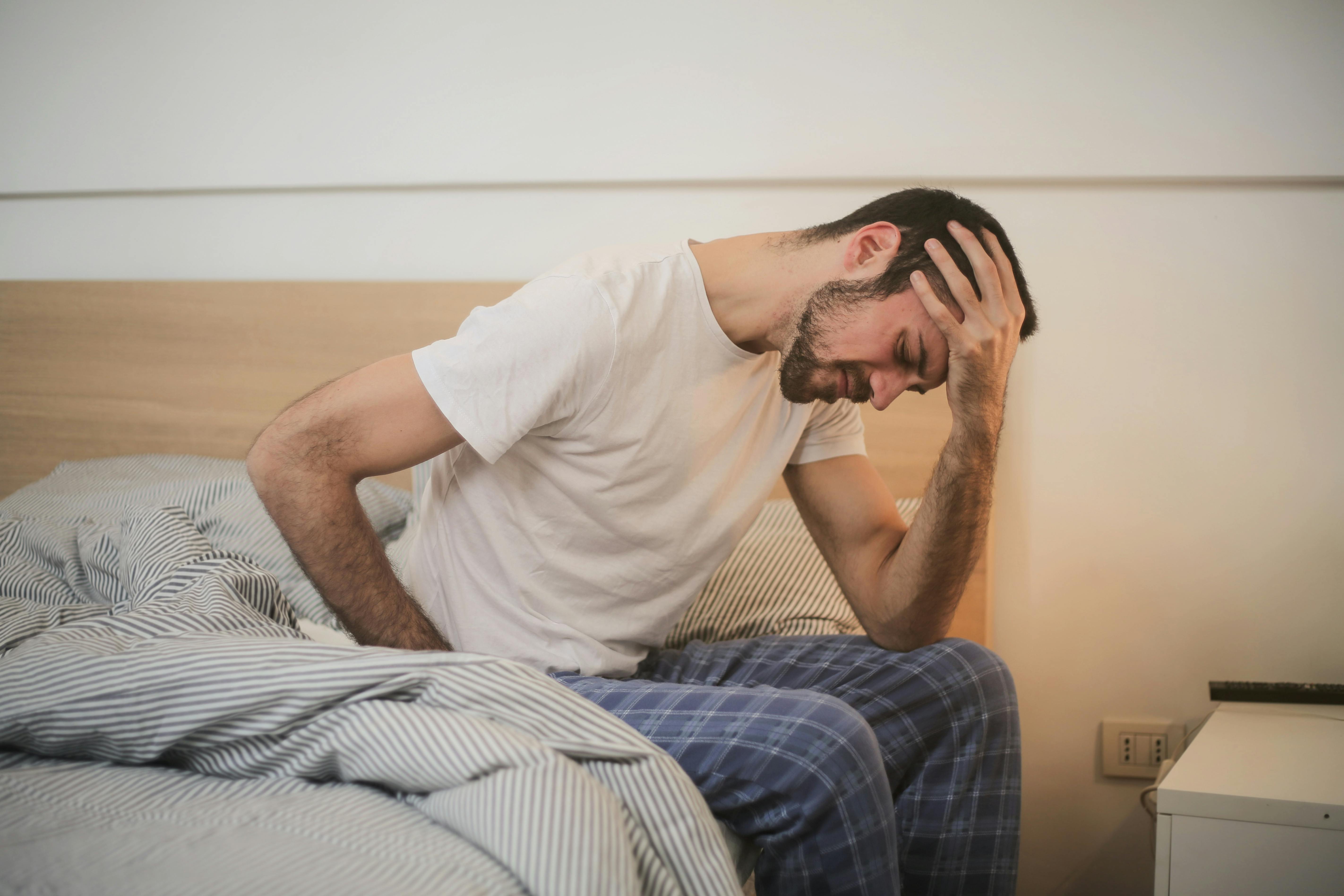 An upset and conflicted man holding his head while sitting on a bed | Source: Pexels