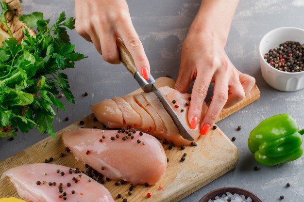 Mujer cortando pechugas de pollo. │Foto: Freepik