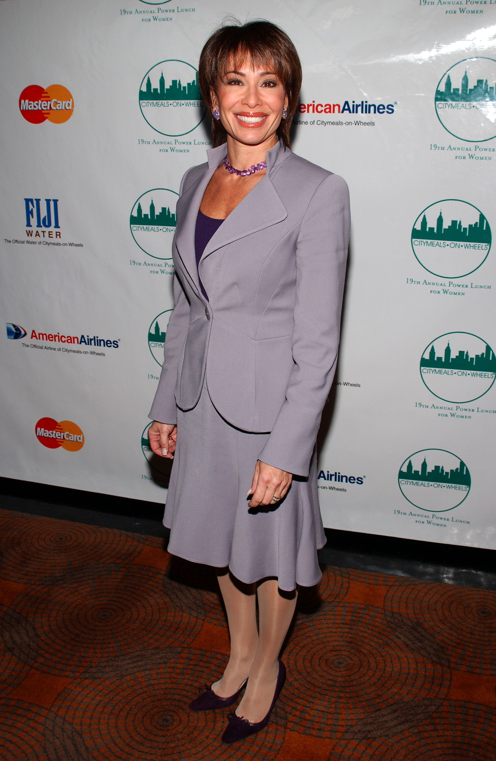 Jeanine Ferris Pirro attends the Citymeals-on-Wheels 19th Annual Power Lunch for Women in New York, wearing a lilac skirt suit with a matching blazer and heels. She smiles warmly on the red carpet.