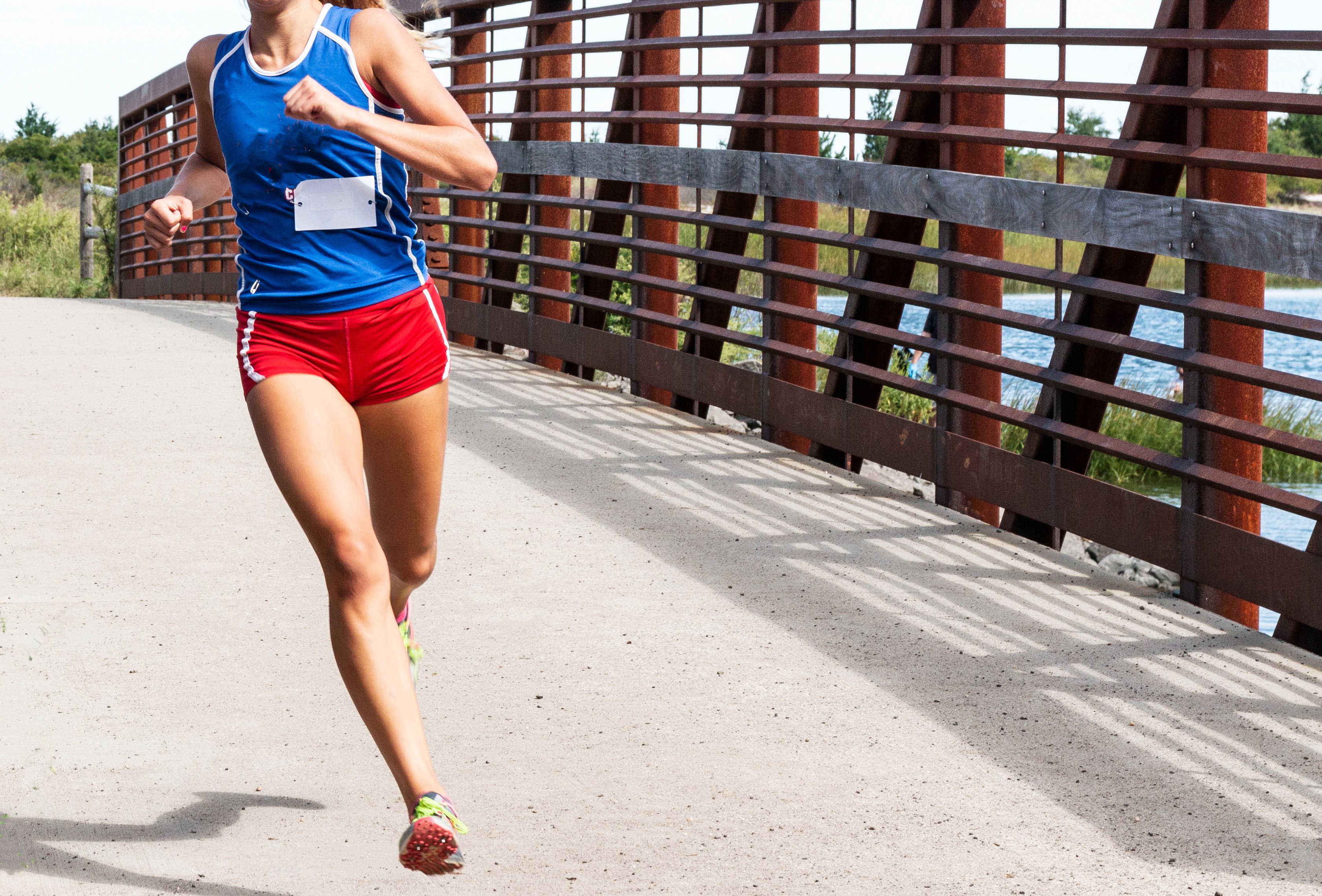 A high school cross country girl is running a race crossing a bridge wearing red shorts and blue racing top | Photo: Shutterstock