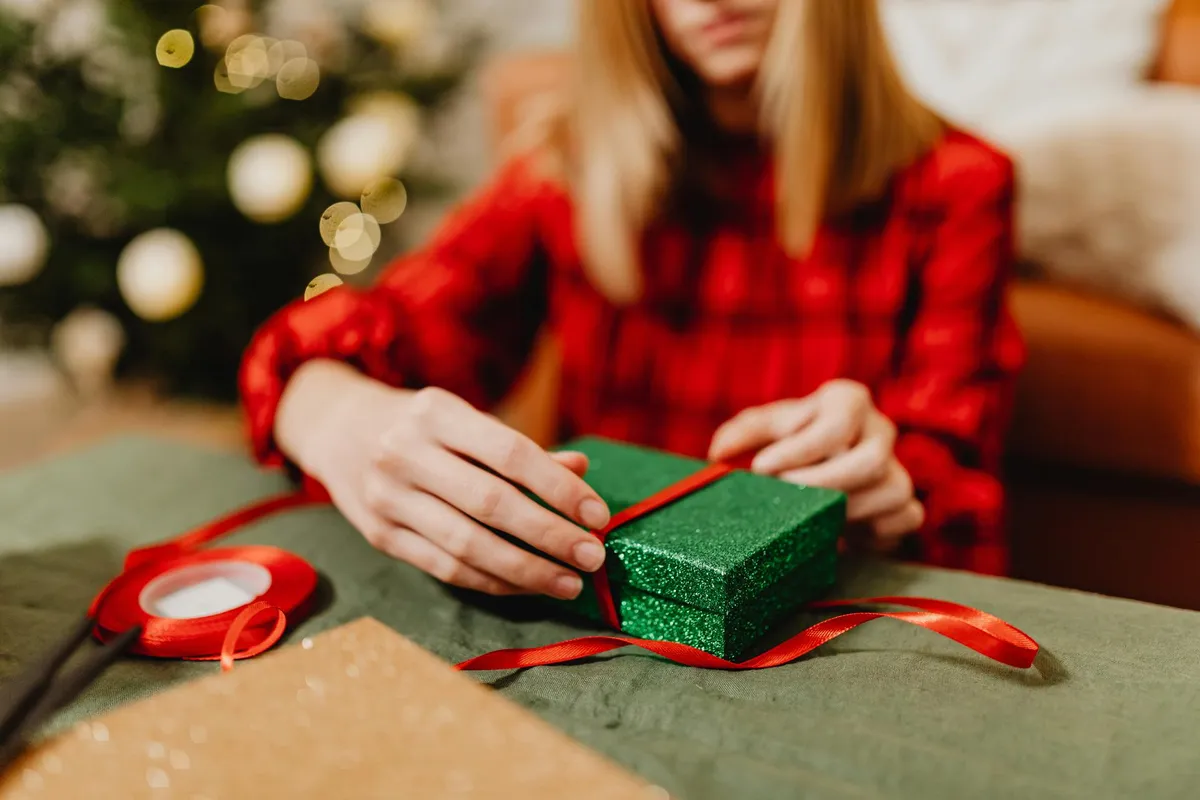 A woman holding a green box with a red ribbon wrapped around it | Source: Pexels