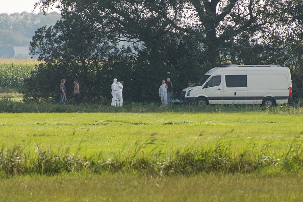Des enquêteurs en combinaison de protection blanche et d'autres personnes se tiennent à côté d'un véhicule de police. |Photo: Getty Images Des enquêteurs en combinaison de protection blanche et d'autres personnes se tiennent à côté d'un véhicule de police. |Photo: Getty Images