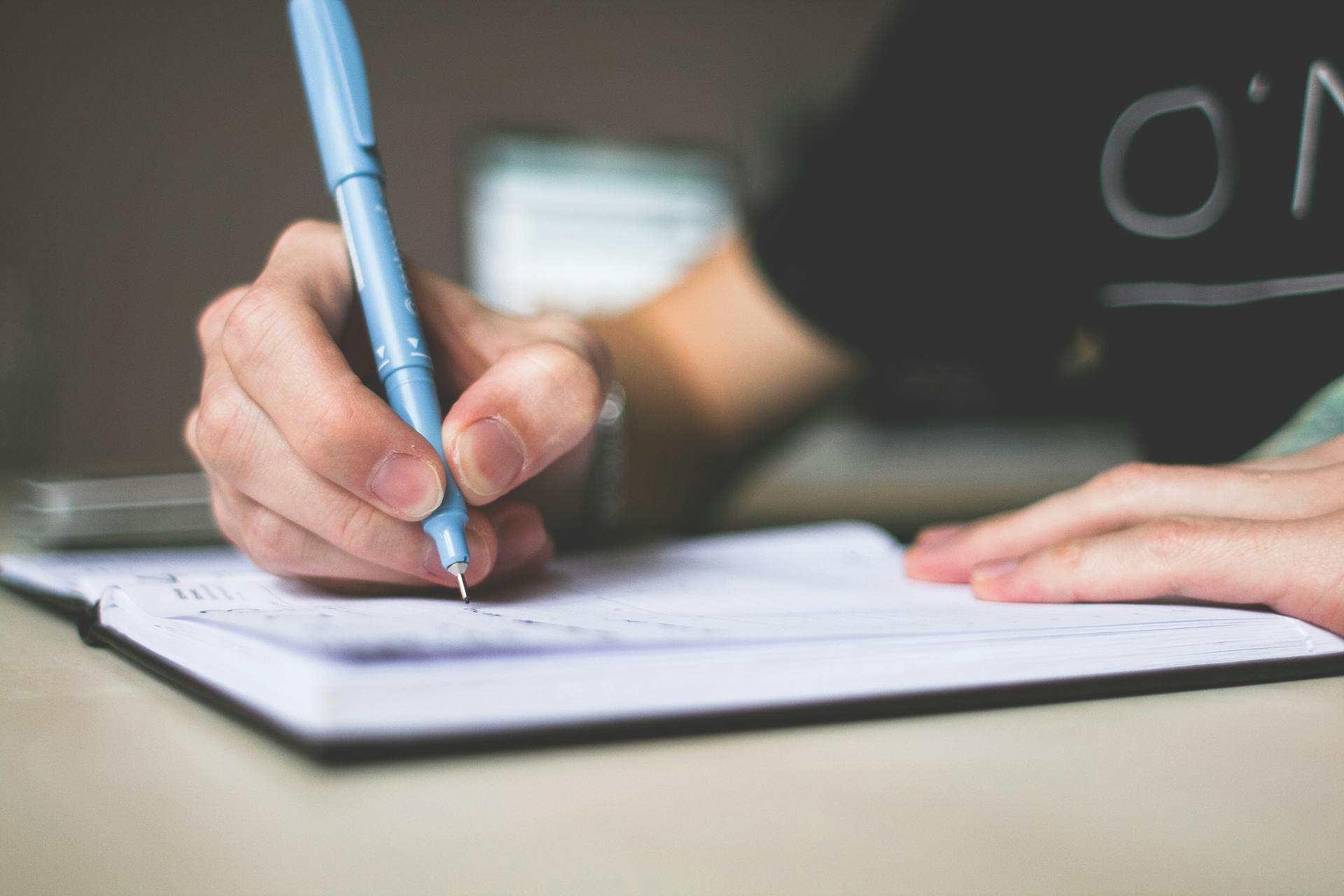 A person writing with a blue ballpoint in their notebook | Source: Pexels