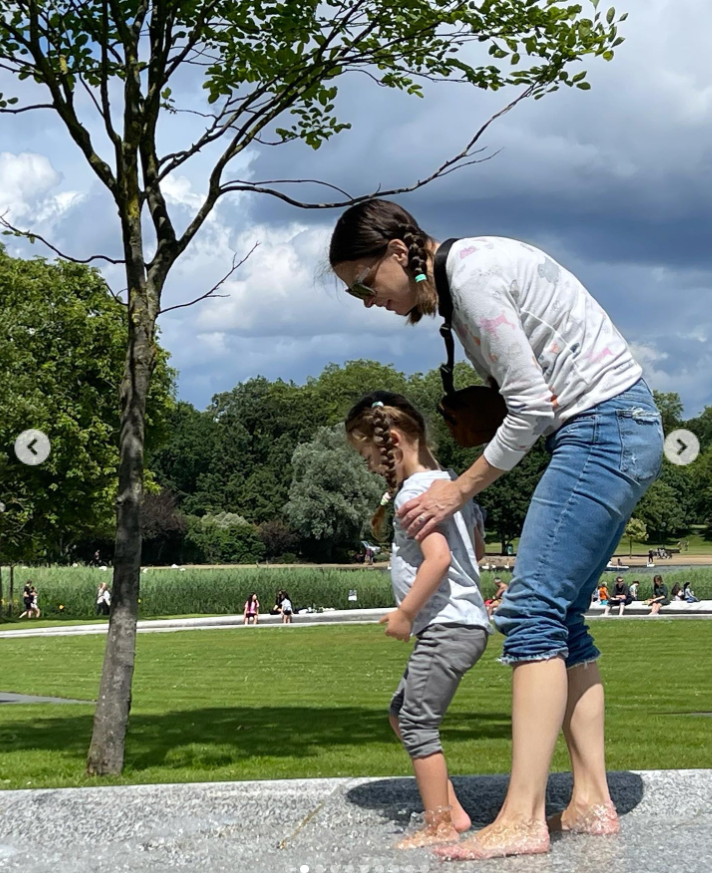 Sutton Foster spends a quiet outdoor moment with her daughter, Emily, beside a shallow fountain in a park. Dressed casually in rolled jeans and a printed sweater, Foster gently steadies the child. | Source: Instagram/suttonlenore