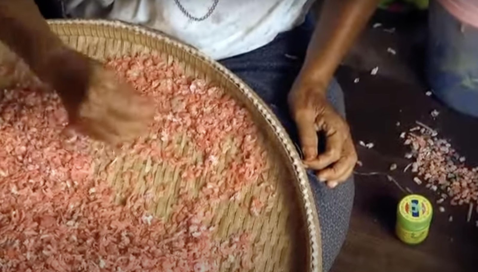 A worker hand-sifts sun-dried shrimp in a woven basket, ensuring the final product meets high artisanal standards. | Source: YouTube/ KRUA dot CO