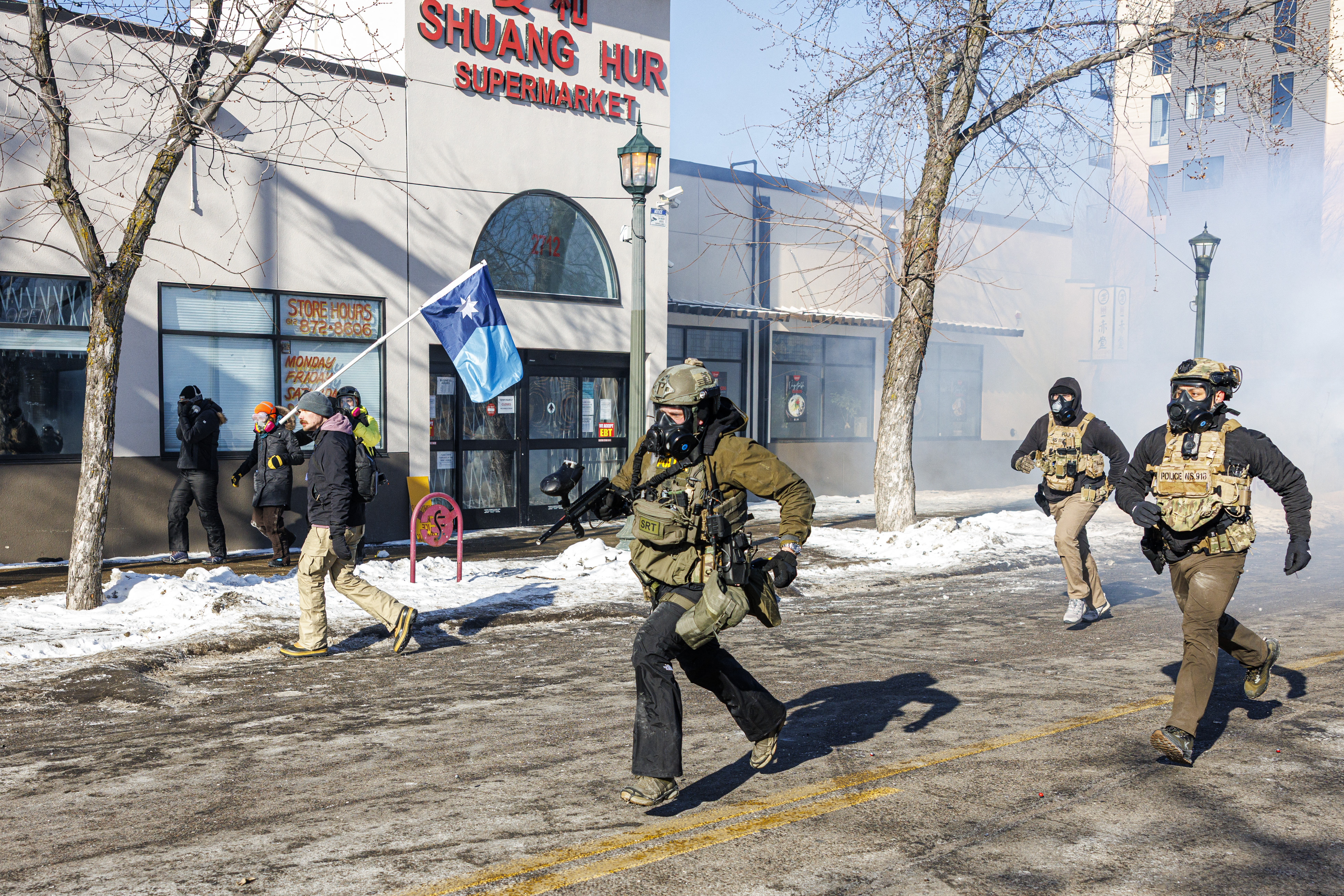 ICE agents run after protesters as a demonstrator carries Minnesota's newly adopted state flag during clashes, on January 24, 2026 in Minneapolis, Minnesota. | Source: Getty Images
