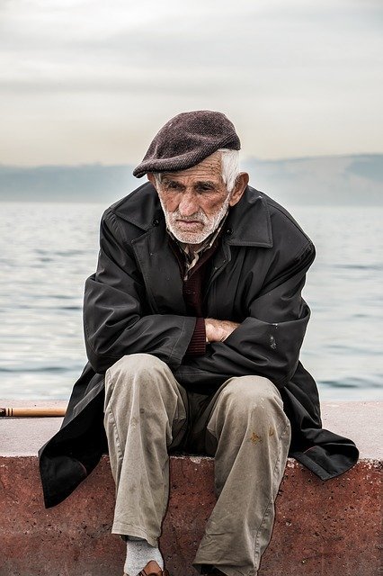 Older man sits by himself in front of the ocean looking down | Photo: PIxabay