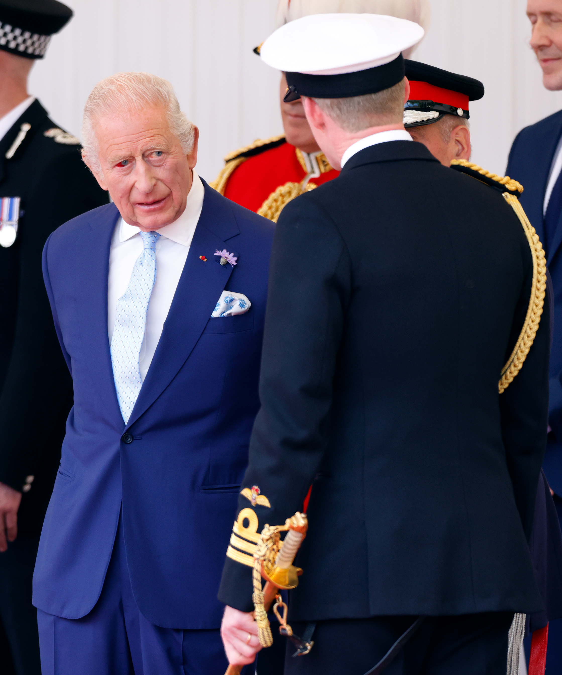 King Charles III engages with uniformed personnel at the formal welcome ceremony in Windsor. His reddened eye is faintly visible as he fulfills his hosting duties with signature poise.