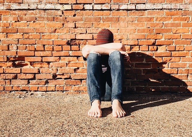 Person sits against brick wall with their heads down in arms | Photo: Pixabay