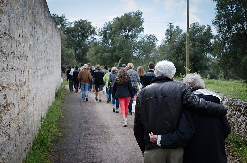Pareja de ancianos caminando detrás de un grupo de gente. | Foto: Wikimedia Commons