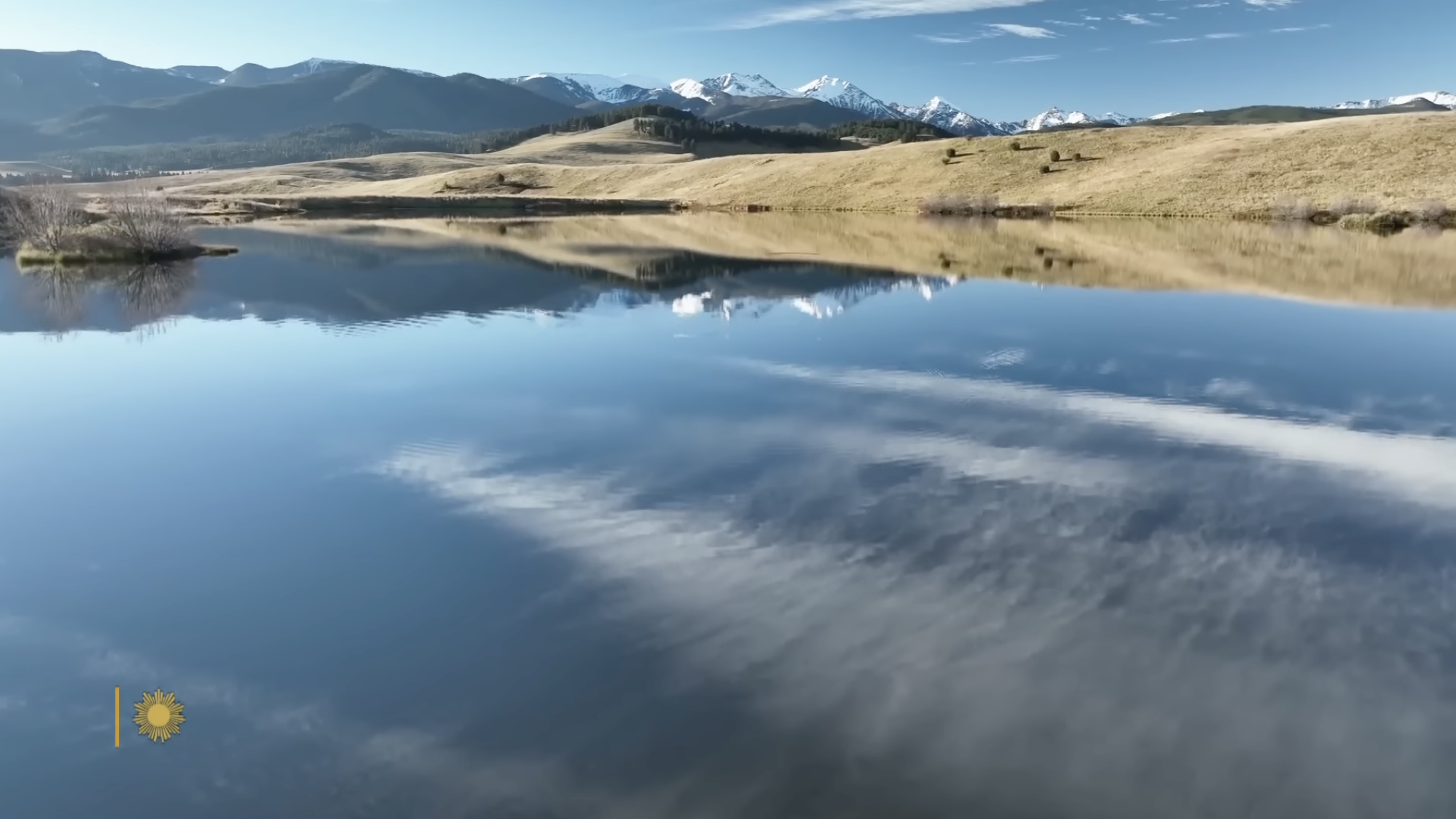 A glassy lake reflects towering mountains and drifting clouds across the serene landscape of Ted Turner’s private conservation land. | Source: YouTube/CBS Sunday Morning